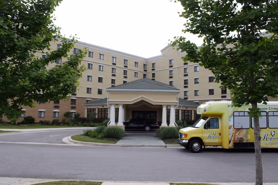 Exterior view of a beige retirement village building with a porte-cochere entrance and yellow bus.