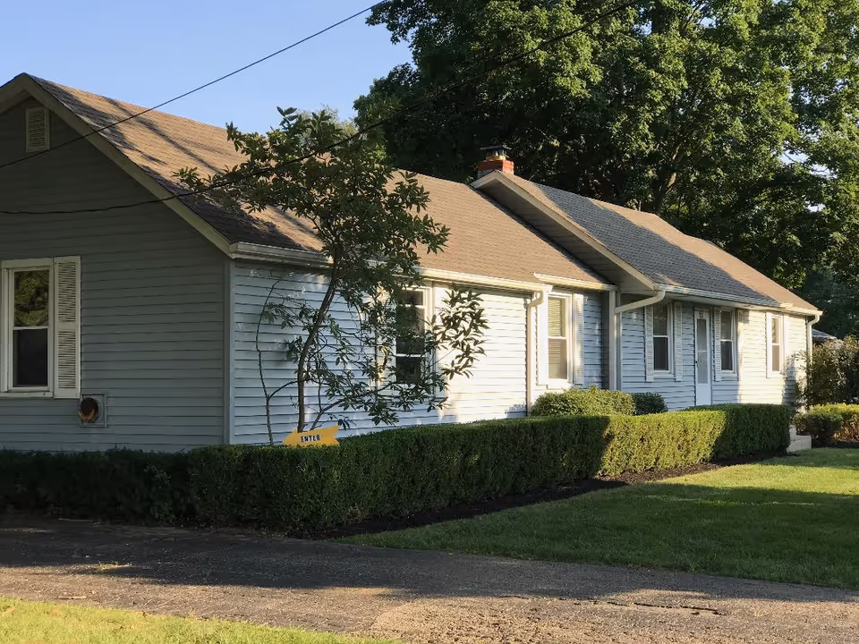 Single-story blue-gray senior living building with trimmed hedges and a driveway.