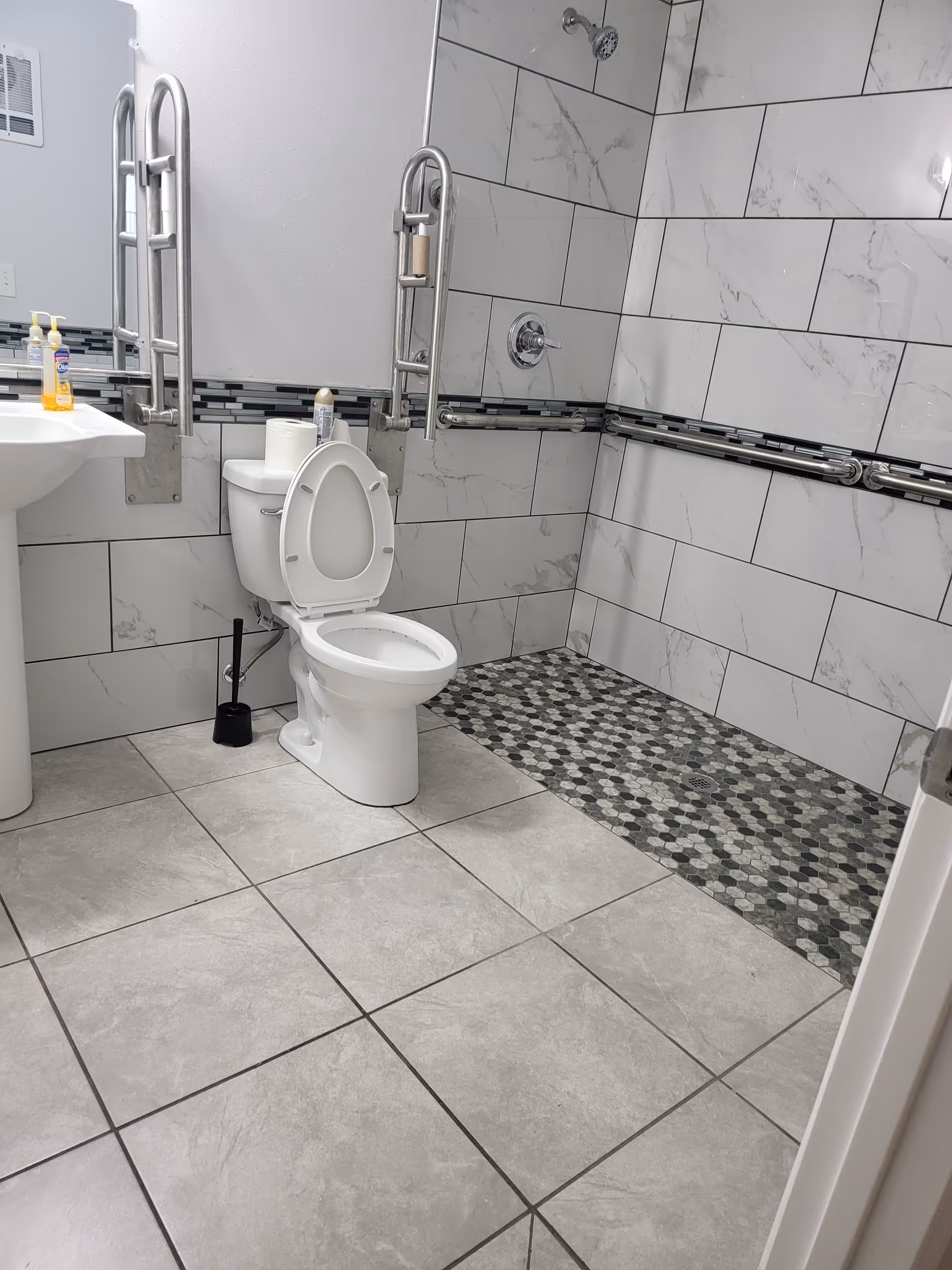 Accessible bathroom with toilet, sink, grab bars, and tiled walls.