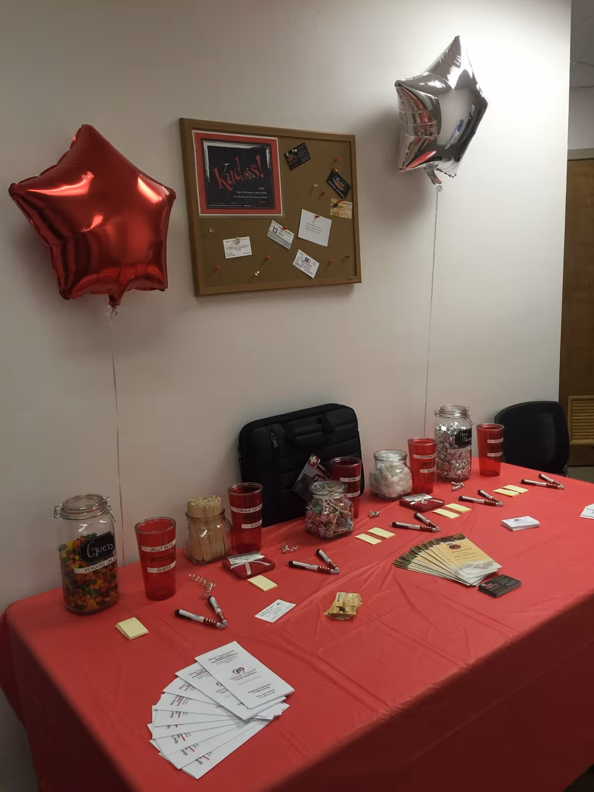 Indoor event setup in a senior living facility: red table, balloons, jars, brochures.