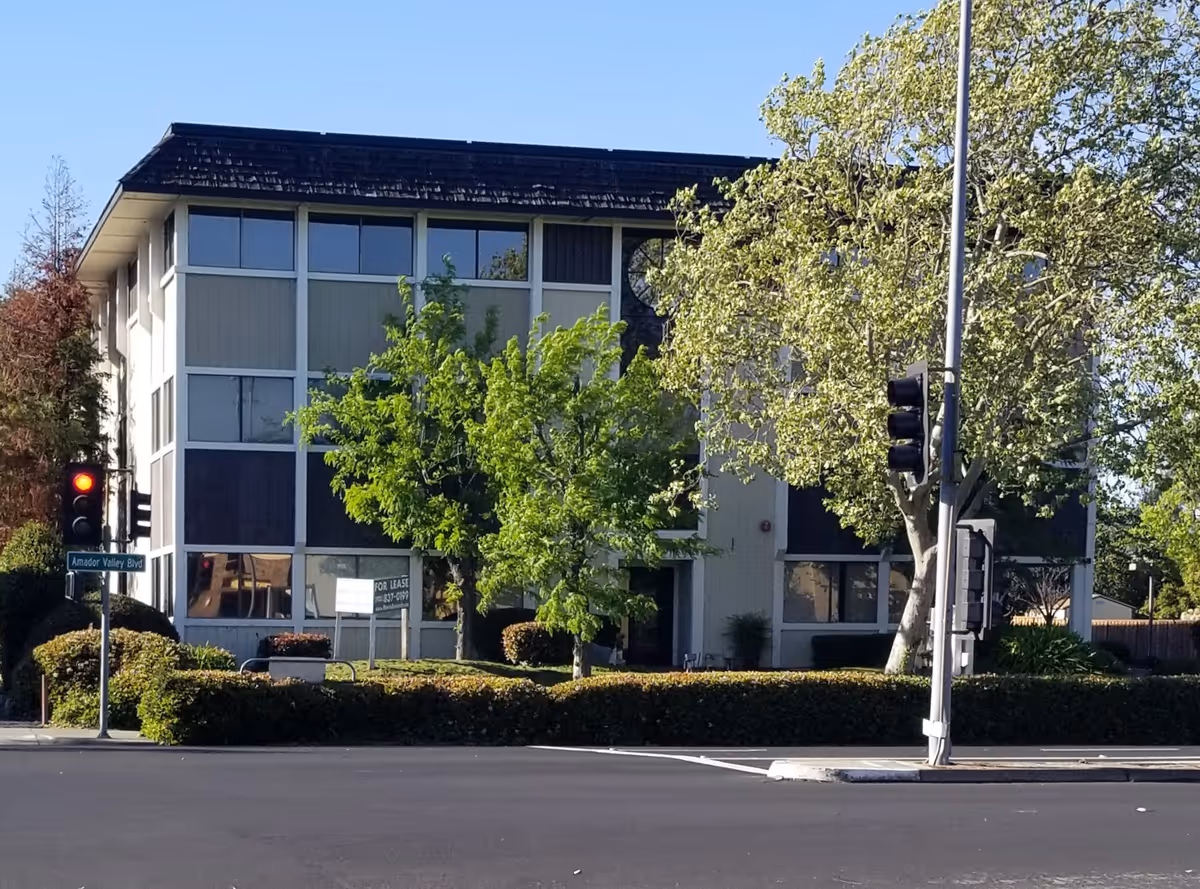 Imagine Home Care building front with large windows, trees, and a traffic light at street corner.