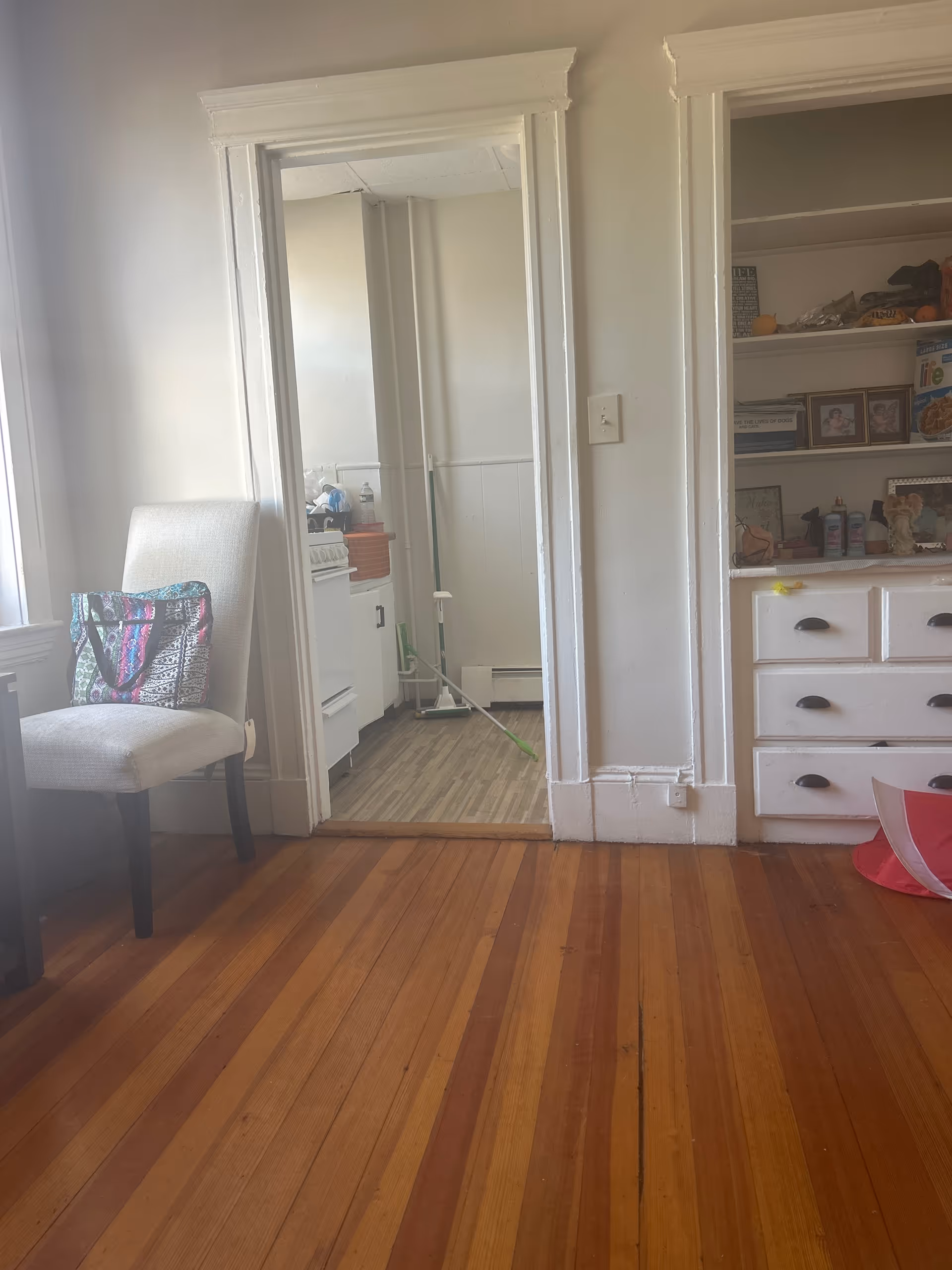 Living room foreground with chair, dresser, and doorway to a small kitchen.