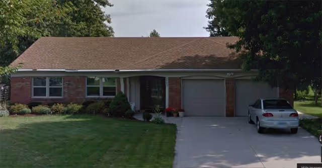 A single-story brick senior living facility with a driveway, lawn, and a parked car.