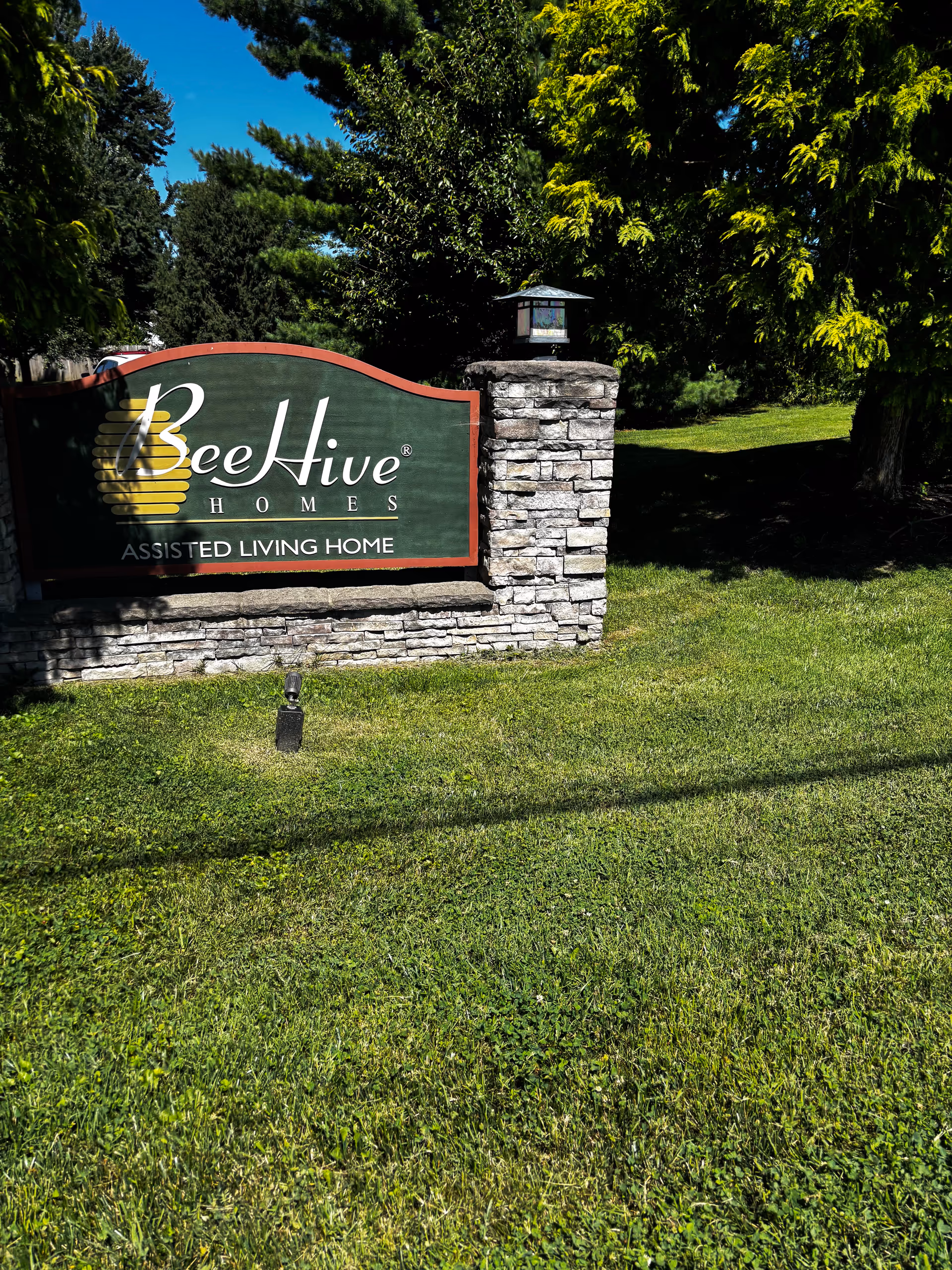BeeHive Homes sign on stone base with green lawn and trees.