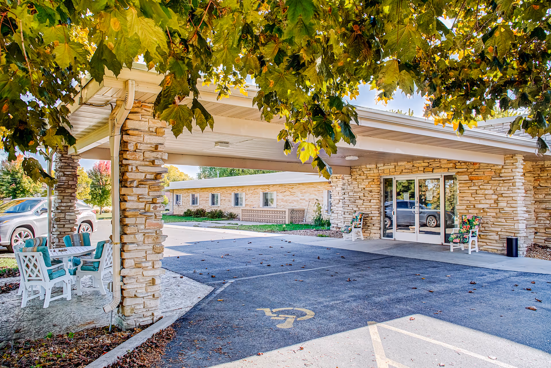Stone-clad entrance with a covered drop-off, stone pillars, and outdoor seating.