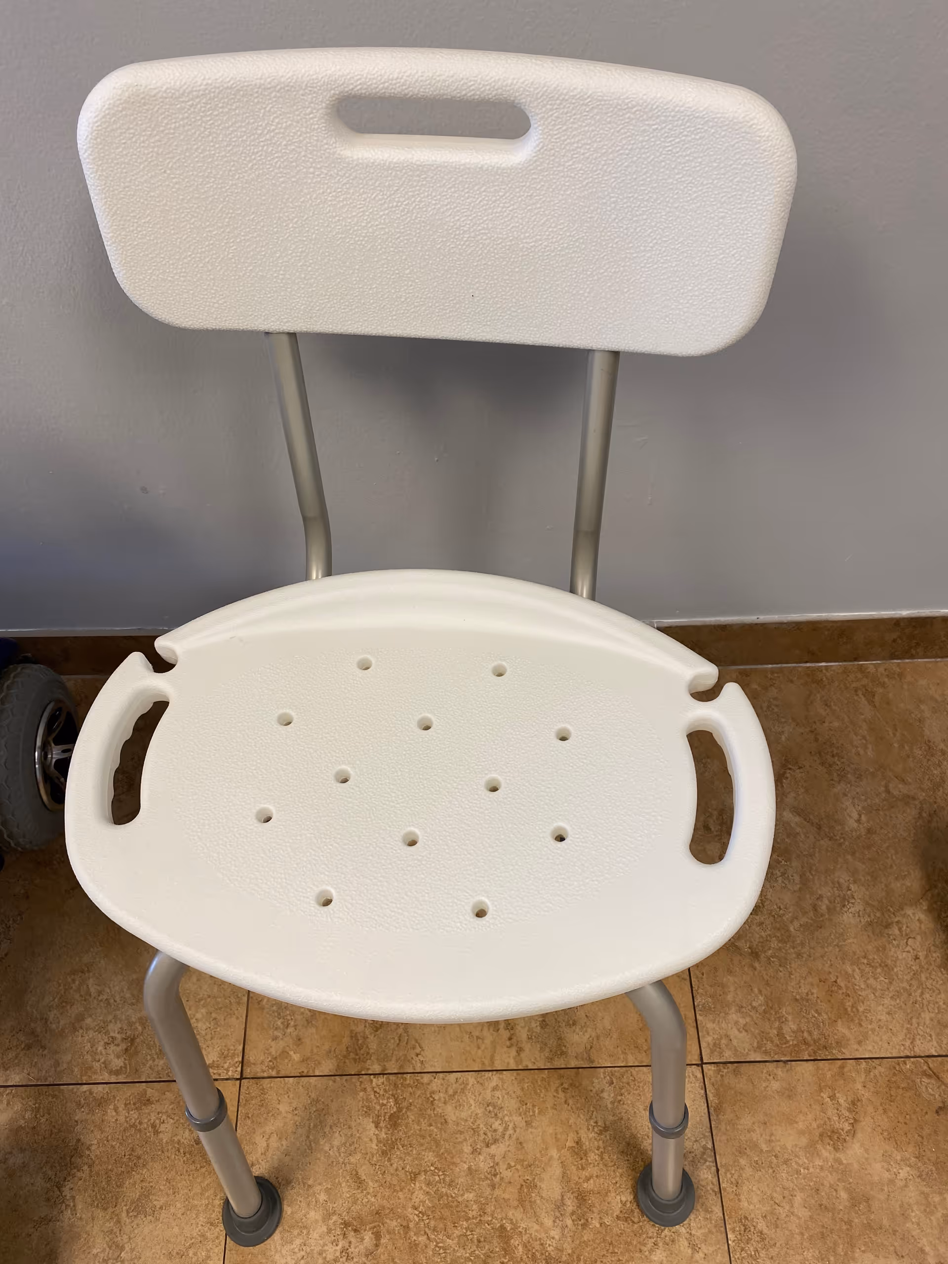 White plastic shower chair with perforated seat and backrest in a tiled interior