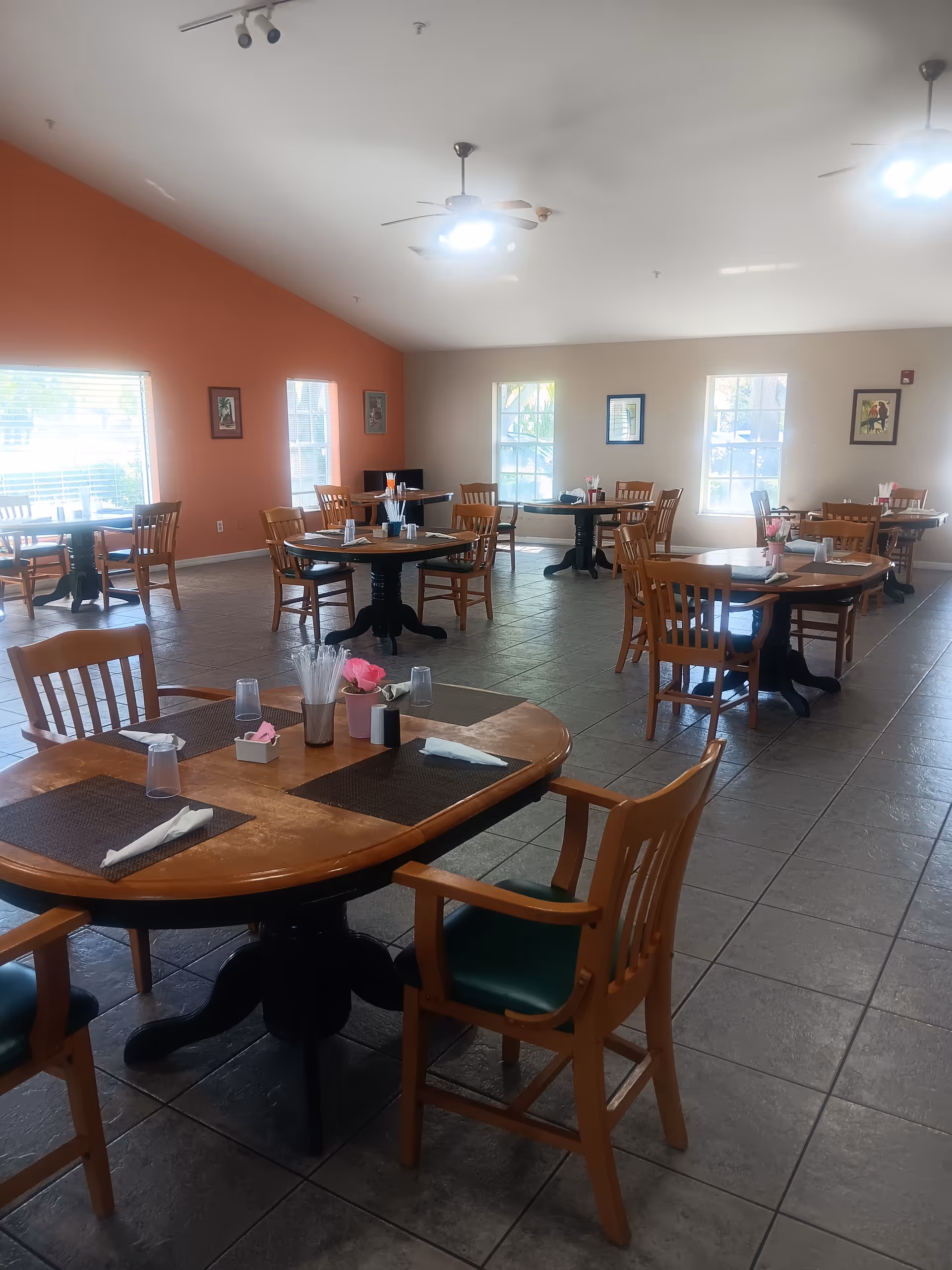 Bright dining room with round tables, wooden chairs, and place settings inside a senior facility.