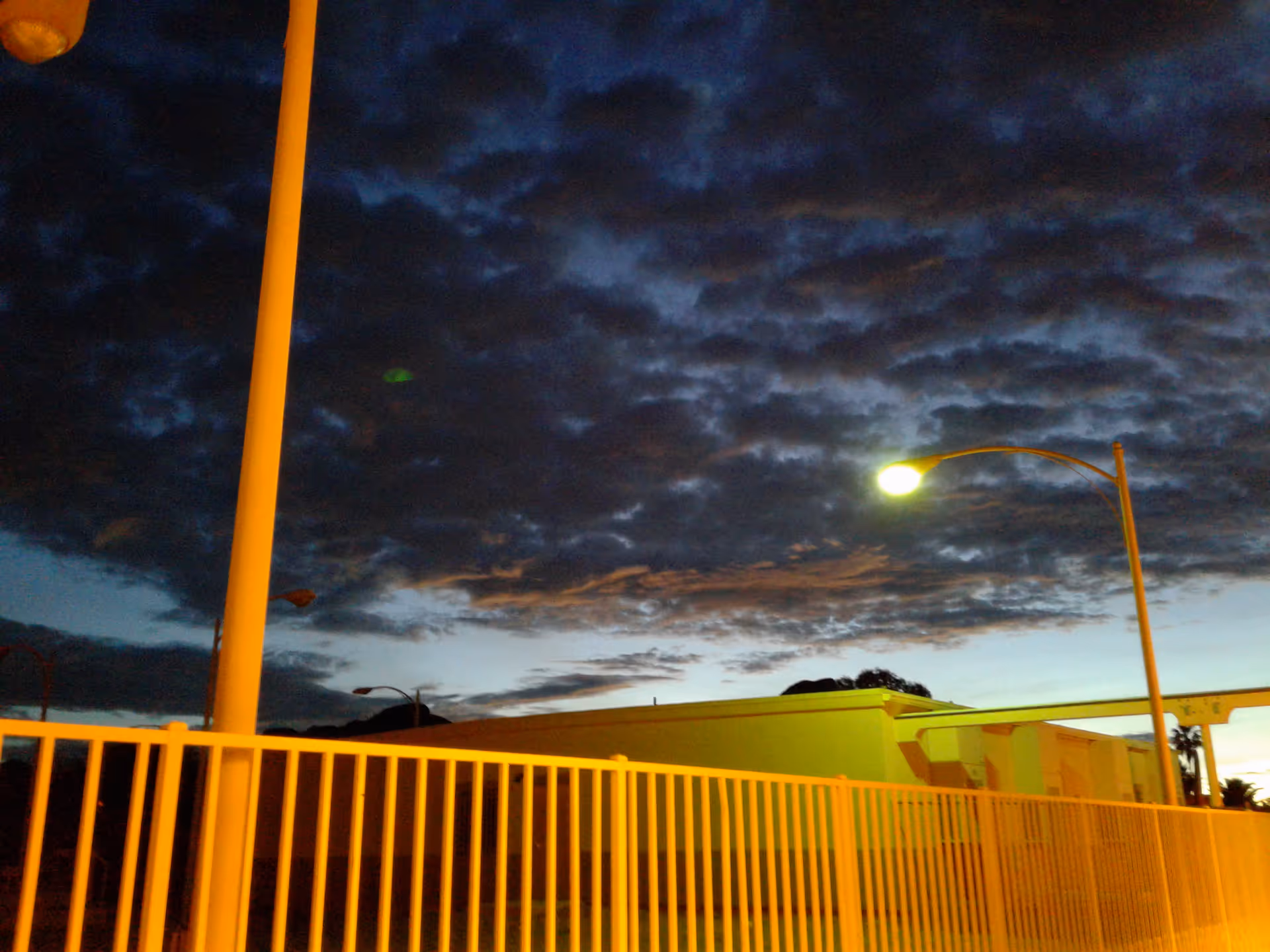 Dusk exterior view of Tucson Estates with a fence, streetlight, and building along the horizon.
