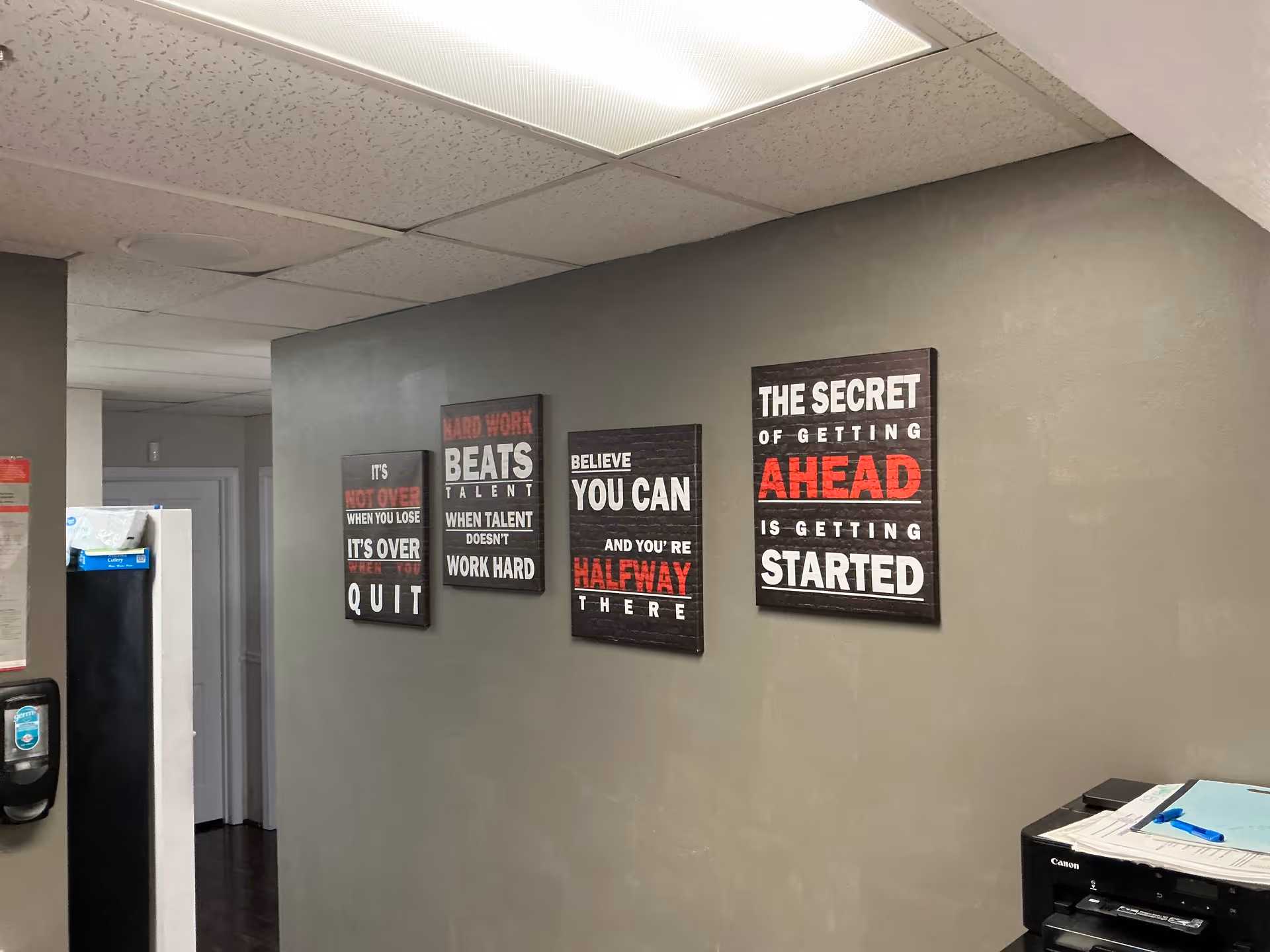 Corridor with gray walls, motivational wall art, and a printer near a water cooler.