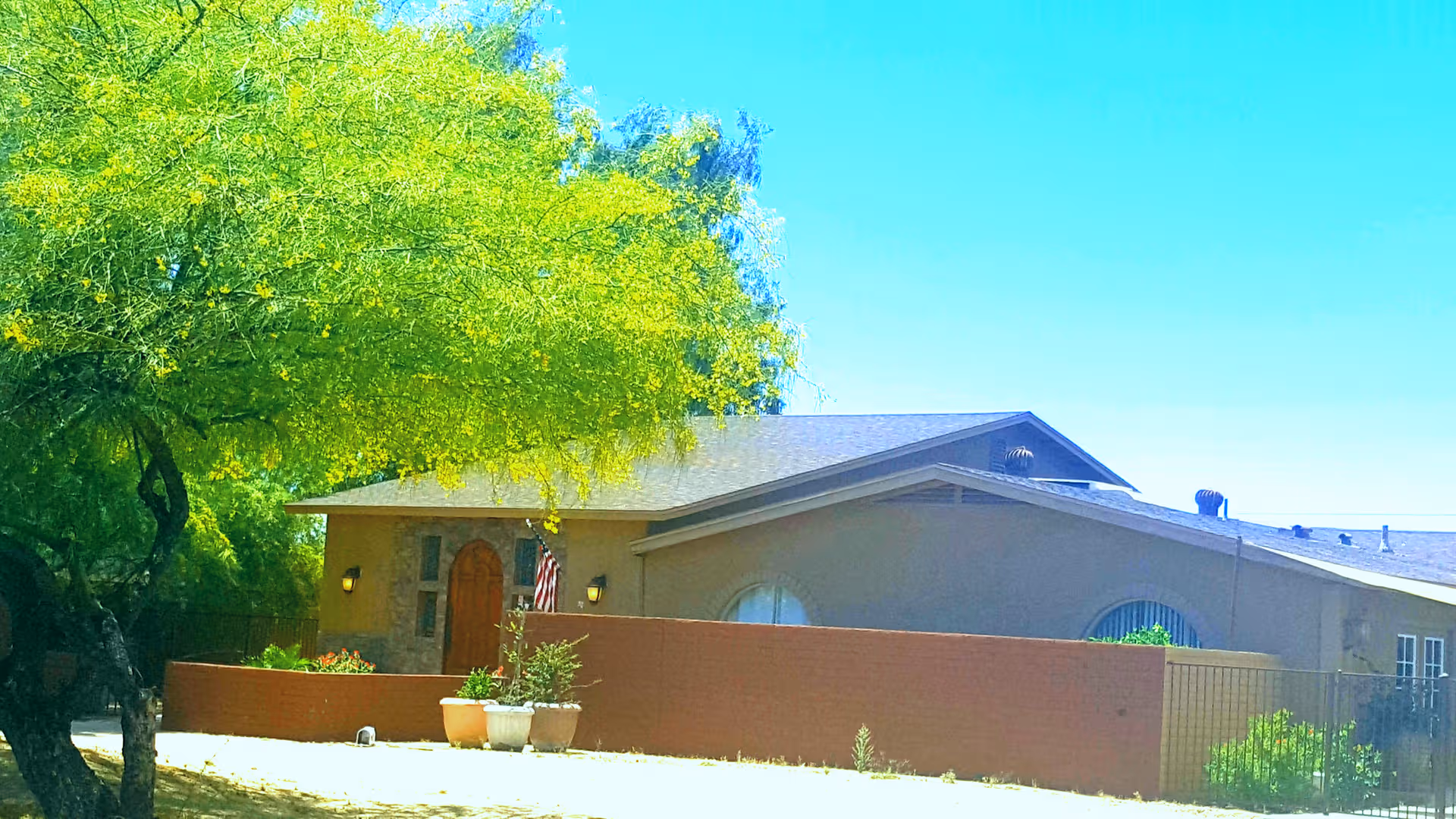 Single-story Sunrise Care Homes Hayden exterior with brick wall, tree, and potted plants.