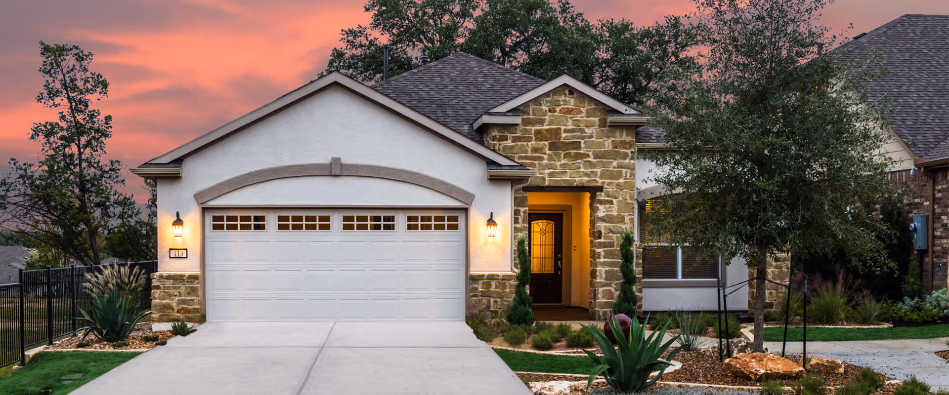A Sun City Texas facility's front exterior featuring a two-car garage and landscaped entry at sunset.