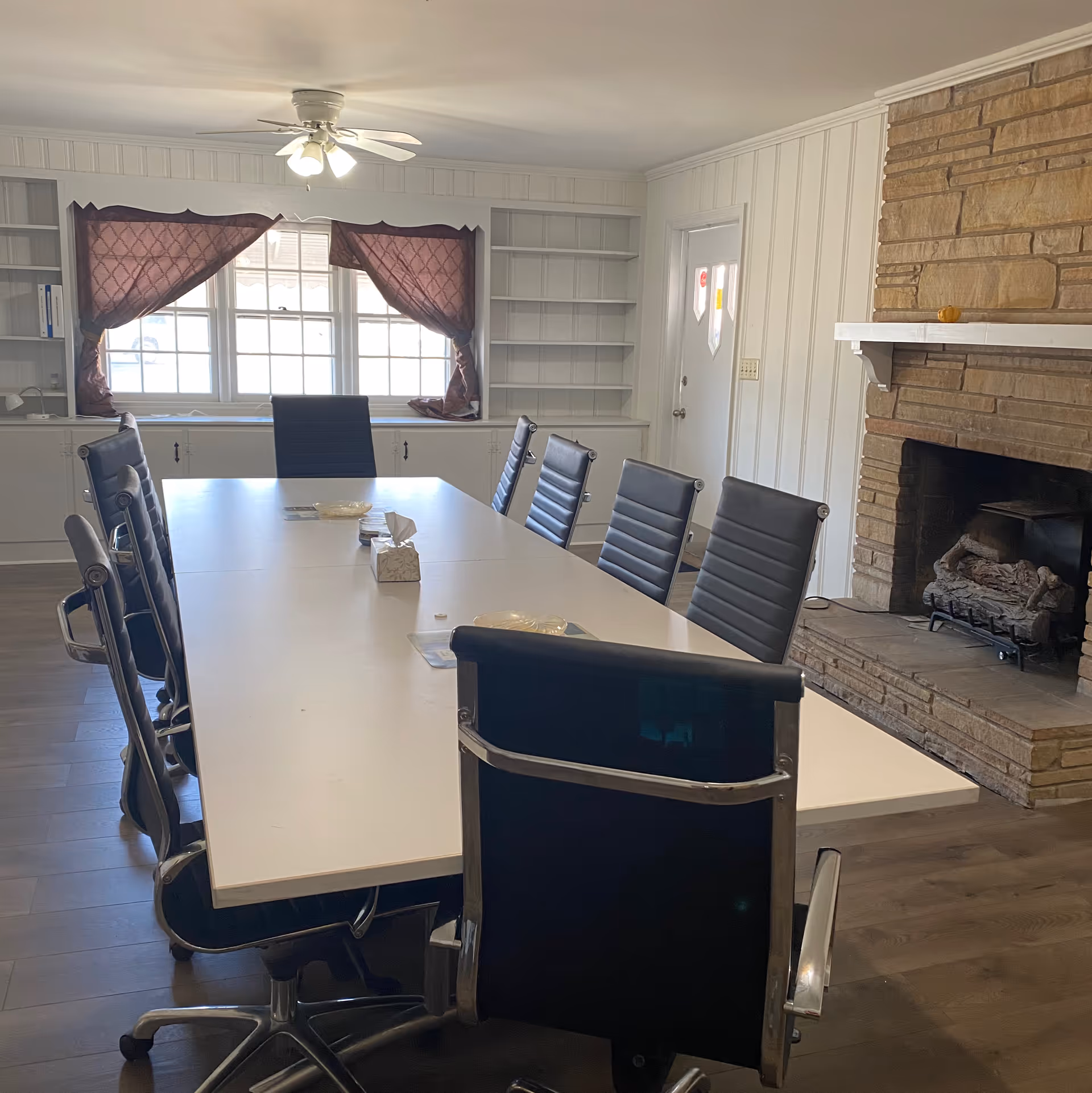 A long white conference table surrounded by black chairs, white panel walls, and a stone fireplace.