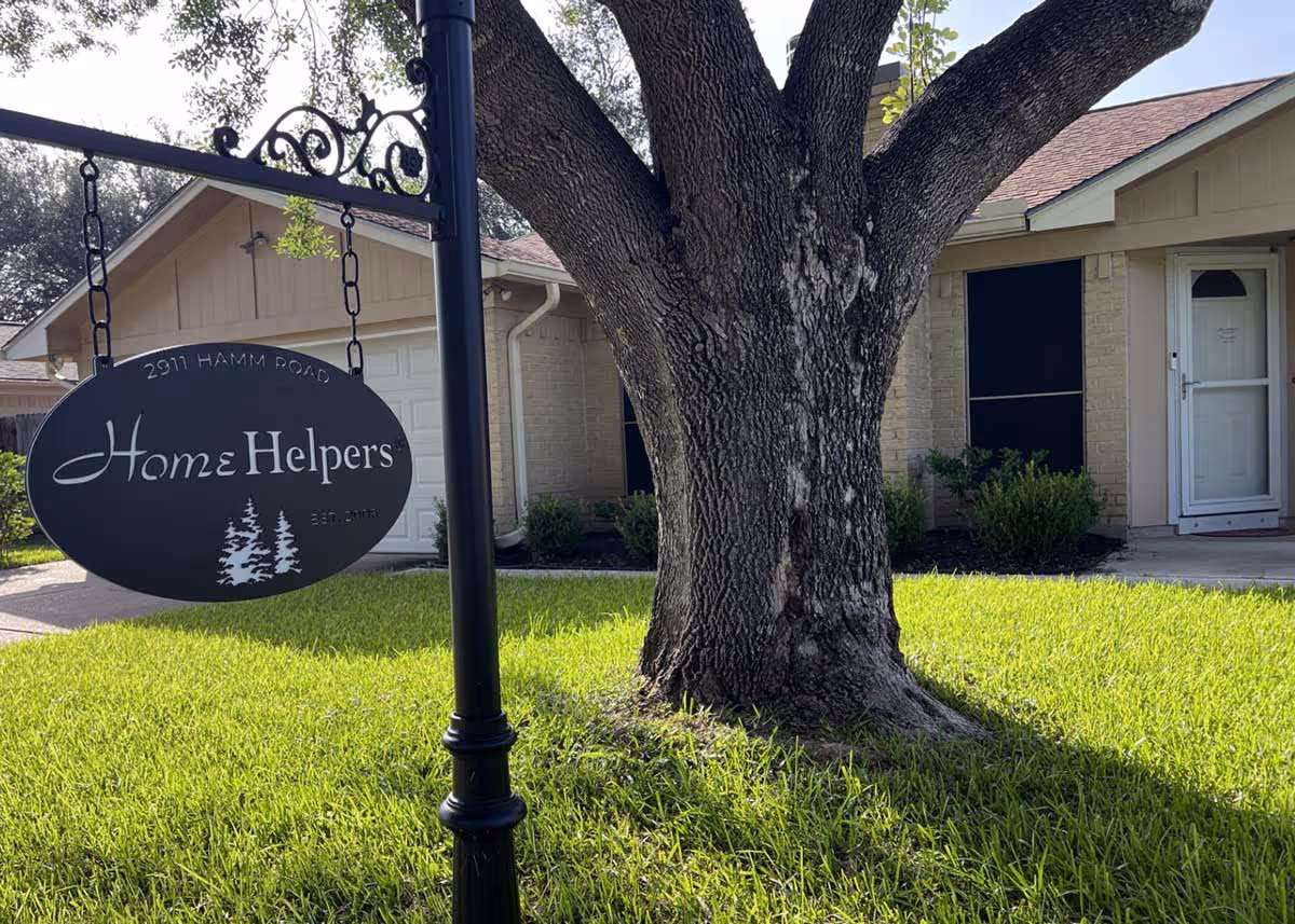 Front exterior of a Home Helpers building with a hanging sign and large tree.
