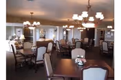 Dining room with many tables, cushioned chairs, chandeliers, and floral centerpieces.