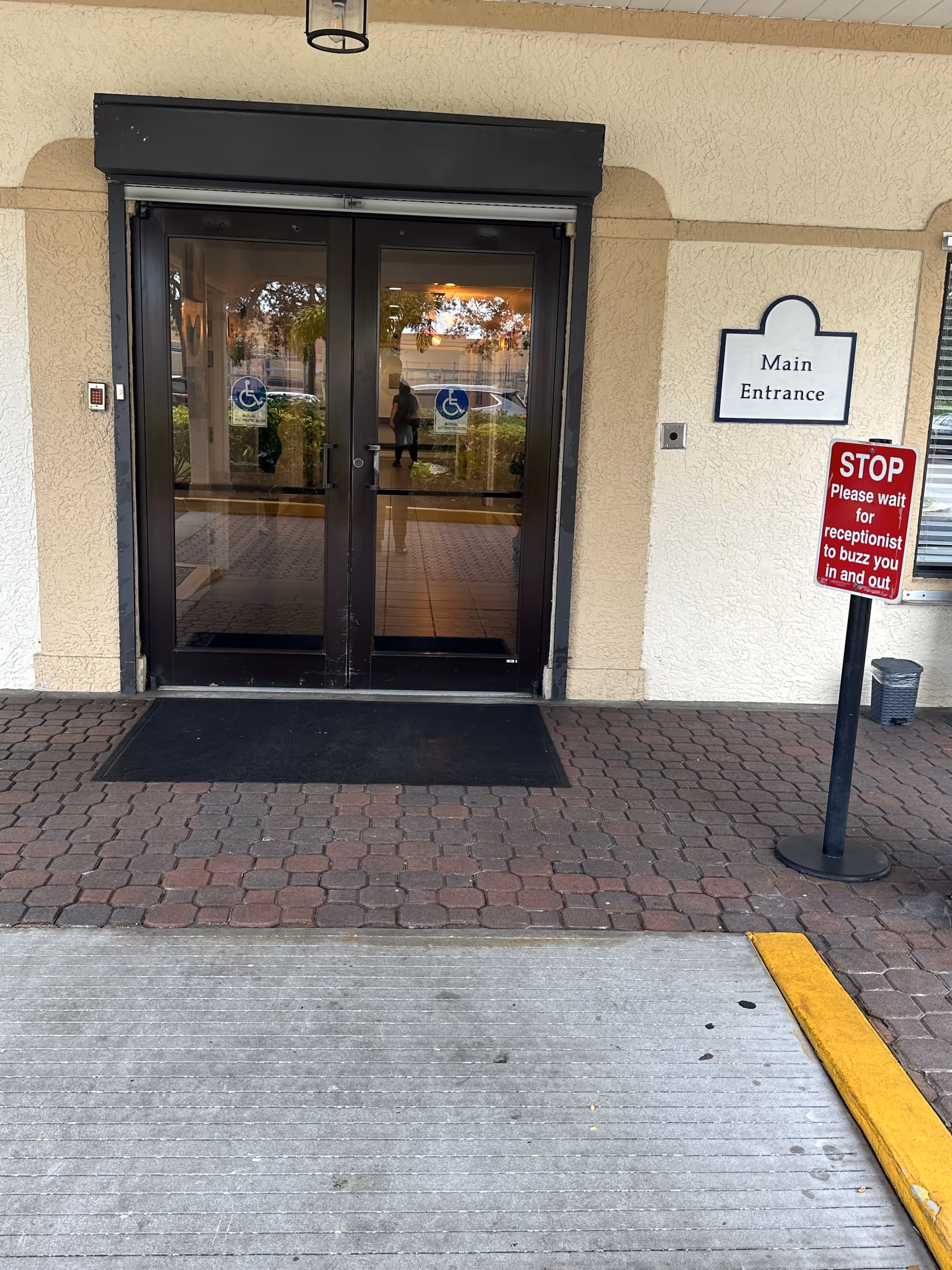 Double glass doors labeled Main Entrance with accessible signs outside a beige building.