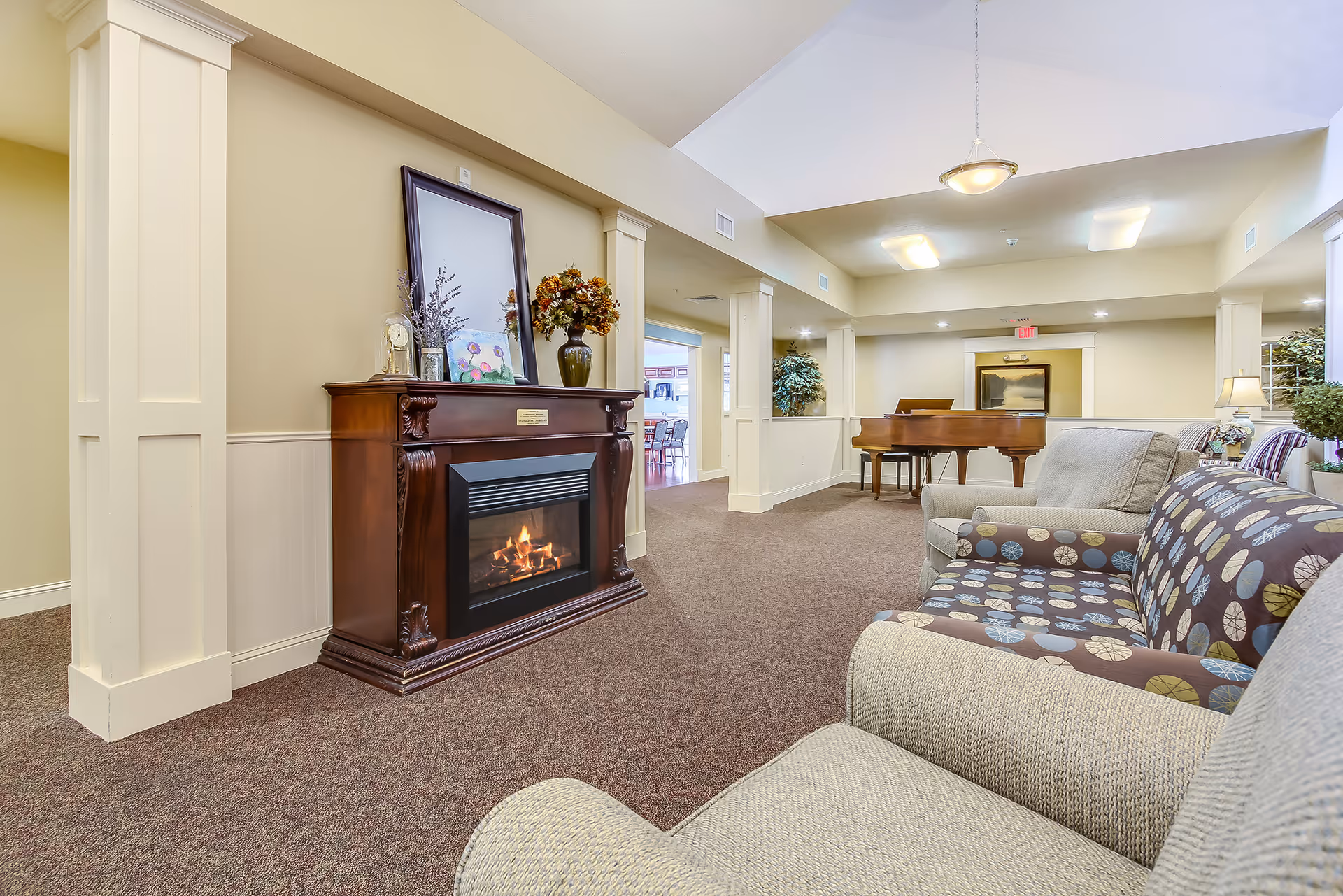 Cozy lounge with fireplace, piano, and patterned seating in a senior living common area.