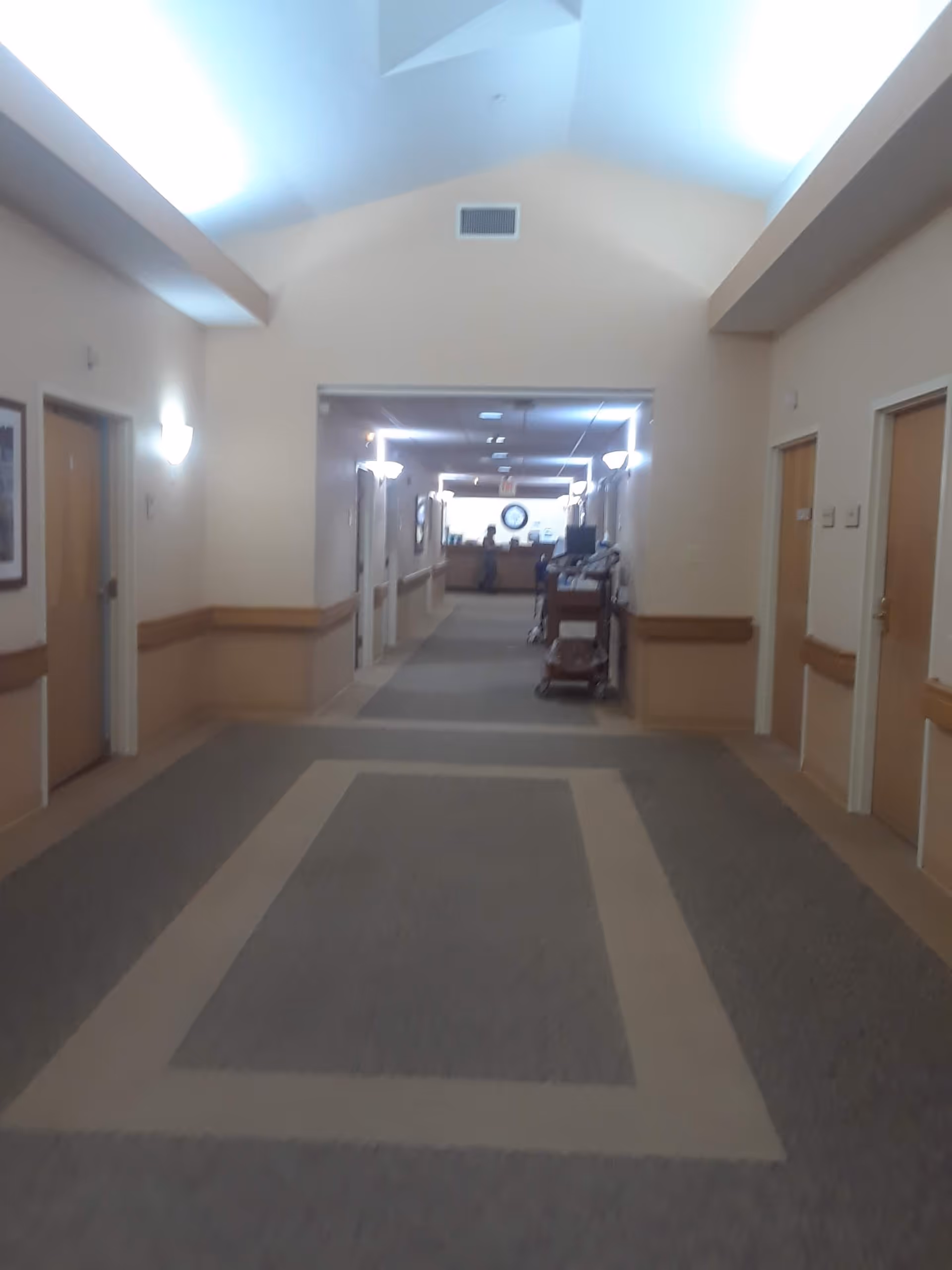 Wide interior hallway in a senior living facility with doors and a cart