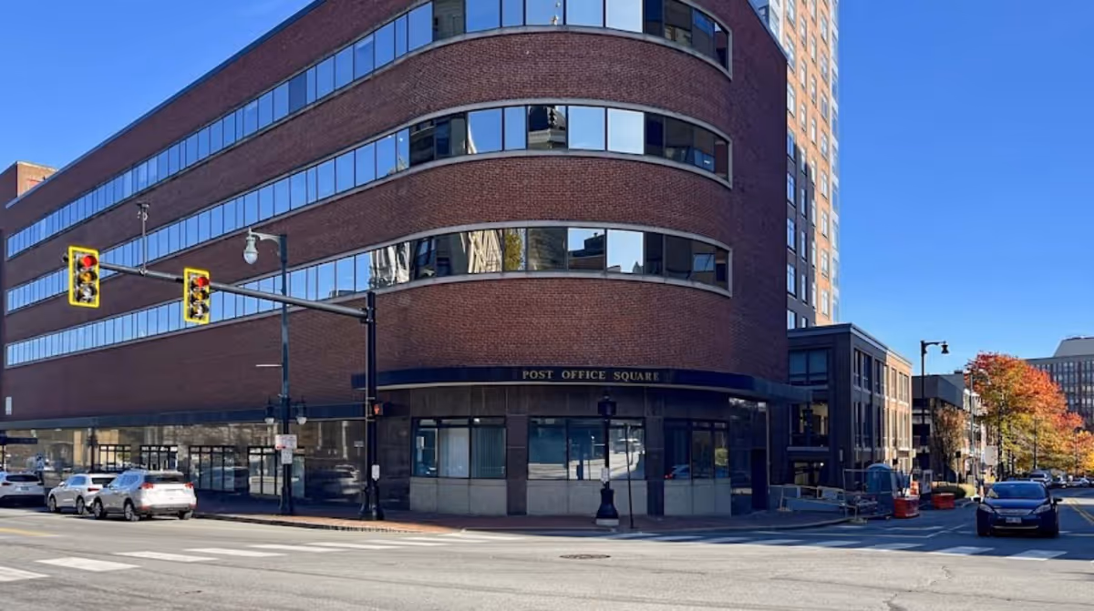 Brick, curved-glass, multi-story building on a street corner with storefront windows.