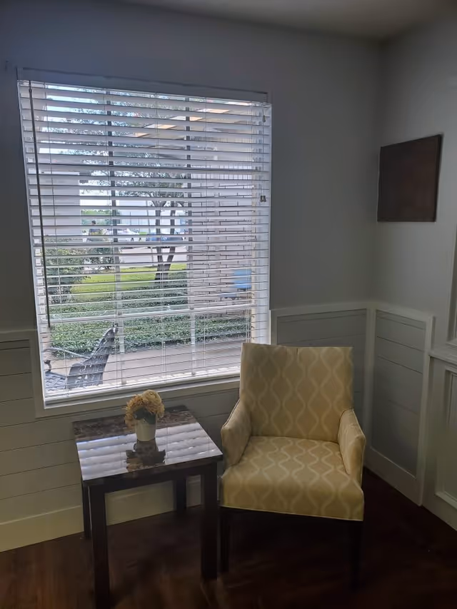 Cozy lounge corner with a patterned chair, small glass table, and window blinds.