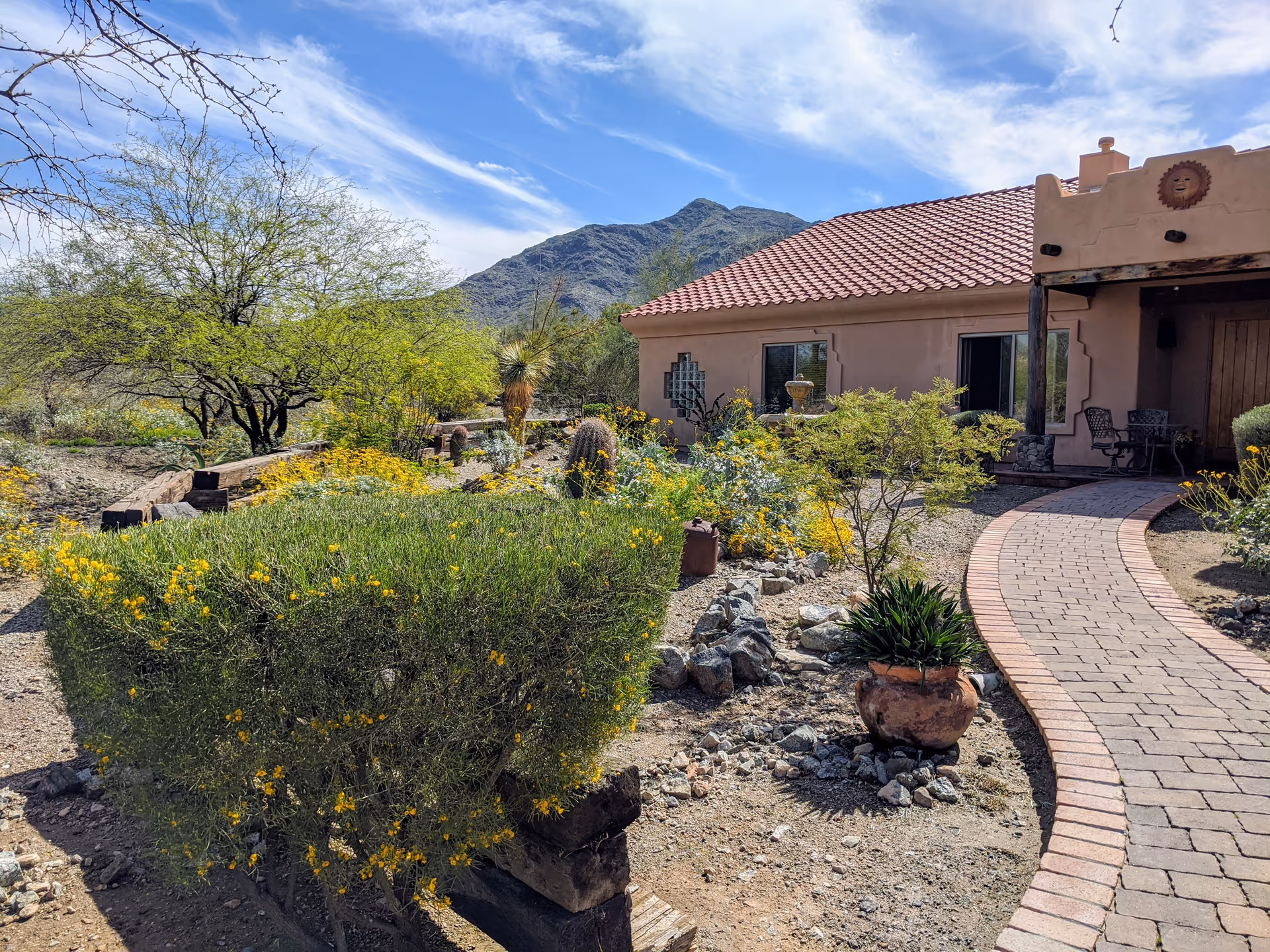 Southwestern-style senior living exterior with a brick walkway, desert landscaping, and mountain backdrop.
