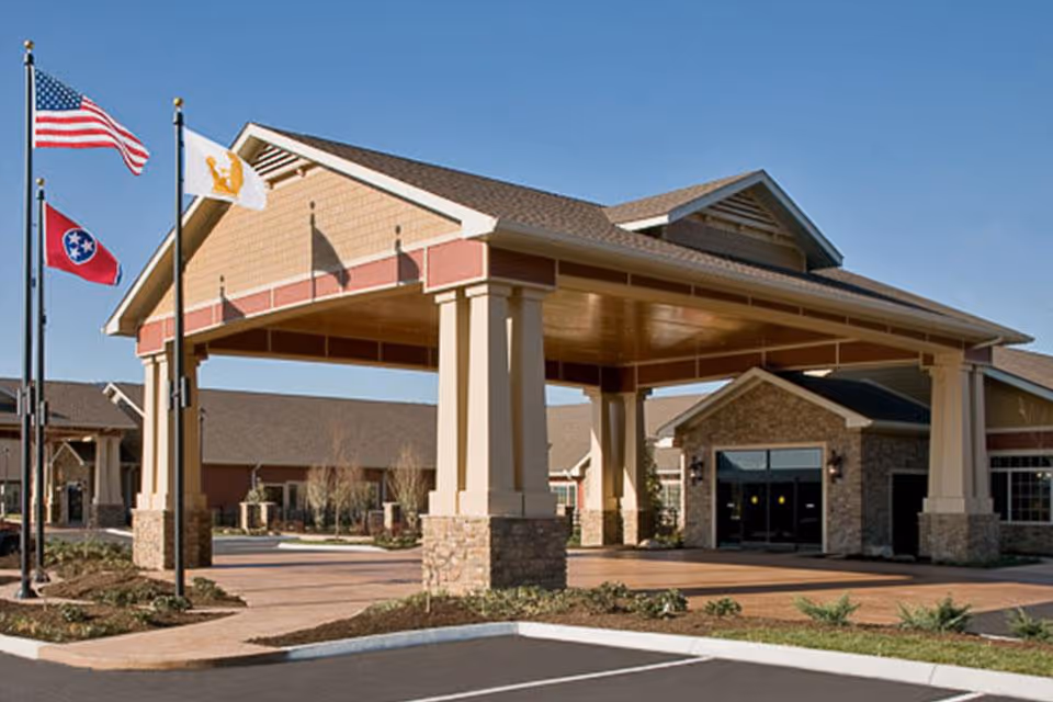 Exterior entrance of a senior living facility with flags and a covered porte-cochère.