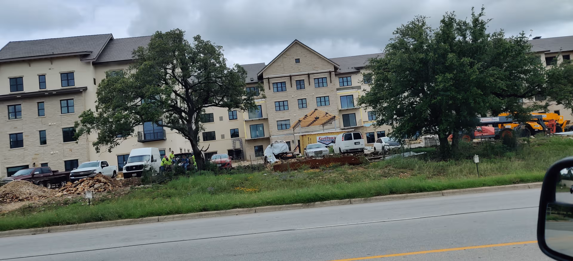 Front view of a multi-story senior living building under construction with trucks and workers.