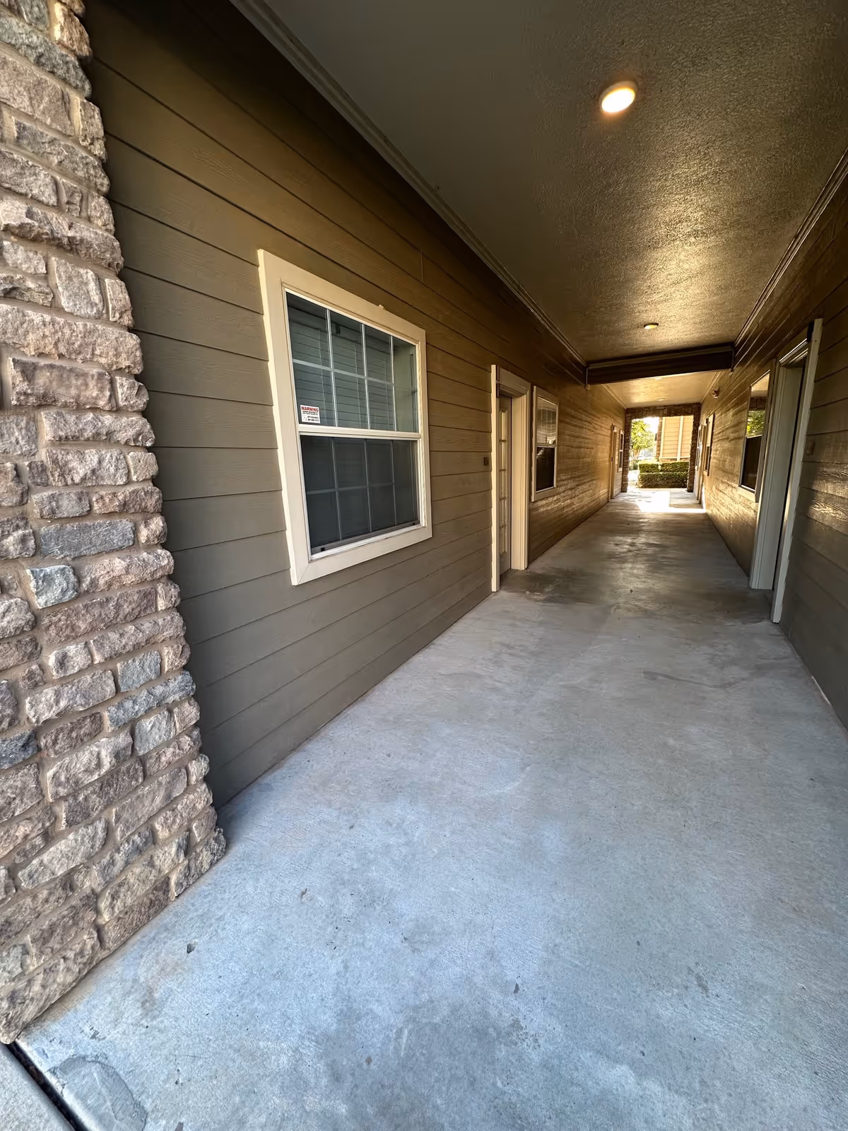 Covered exterior corridor of a senior living building with windows, doors, and stone wall.