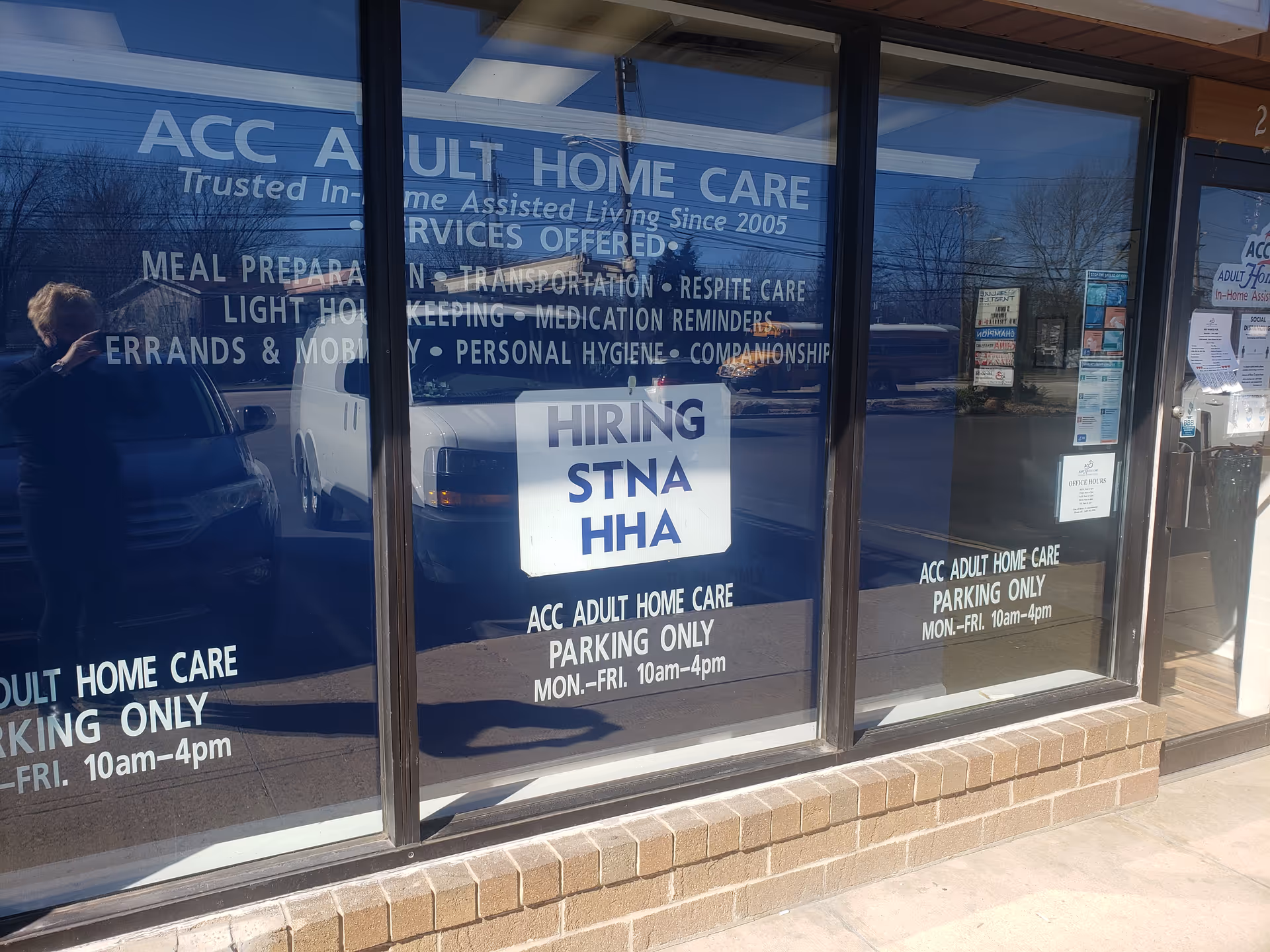 Front of ACC Adult Home Care storefront with large window signs and a hiring sign.