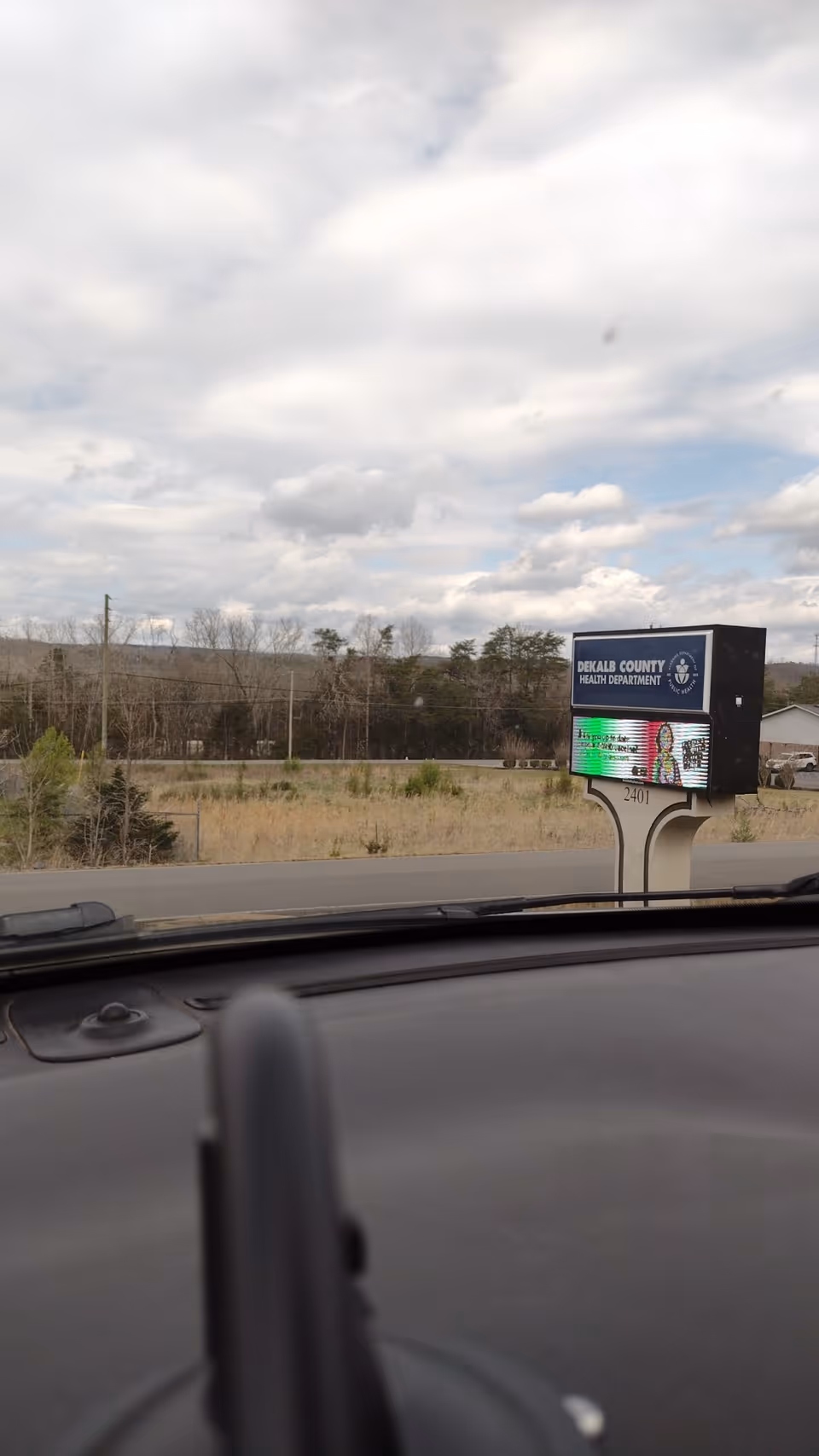 From inside a car, sign reads DeKalb County Health Department beside a rural road.