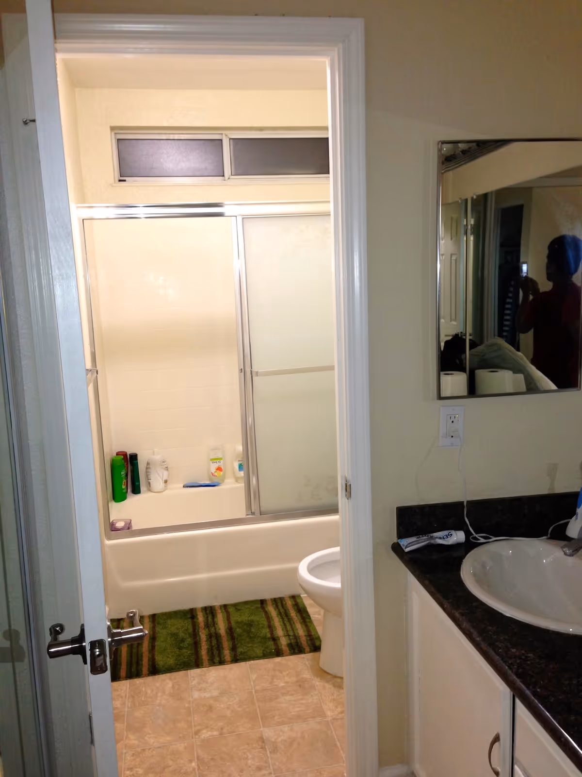 Bathroom in a residential care facility with shower, sink, mirror, and toiletries.