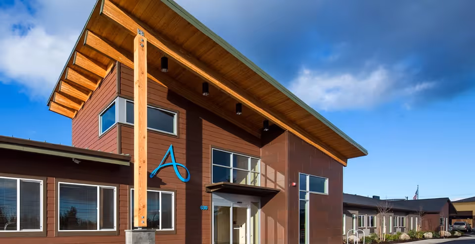 Modern facility front exterior with brown panels, blue logo, and wooden overhang.