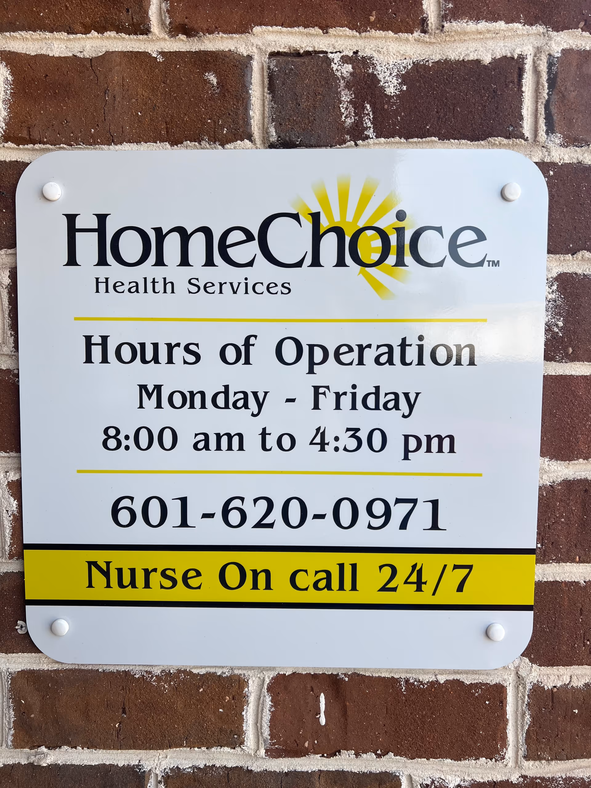 Exterior brick wall sign advertising HomeChoice Health Services hours and 24/7 nurse line.