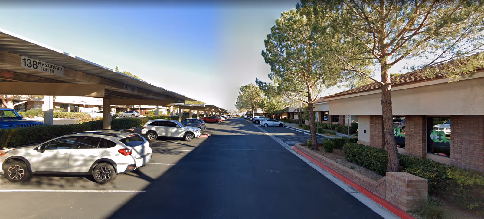 Exterior view of a senior facility parking lot with carports, cars, and trees.