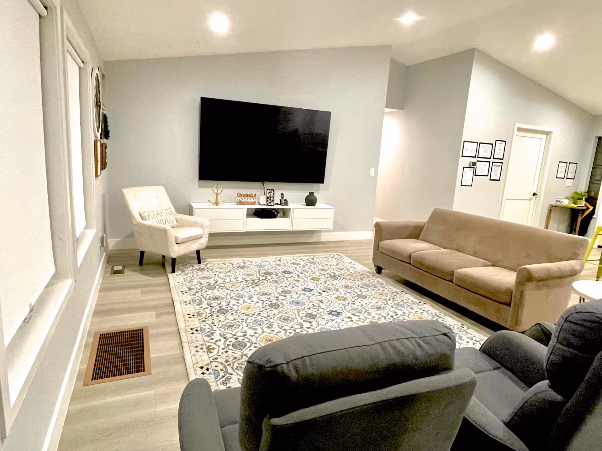Cozy living room with a wall-mounted TV, beige sofas, and a patterned rug.
