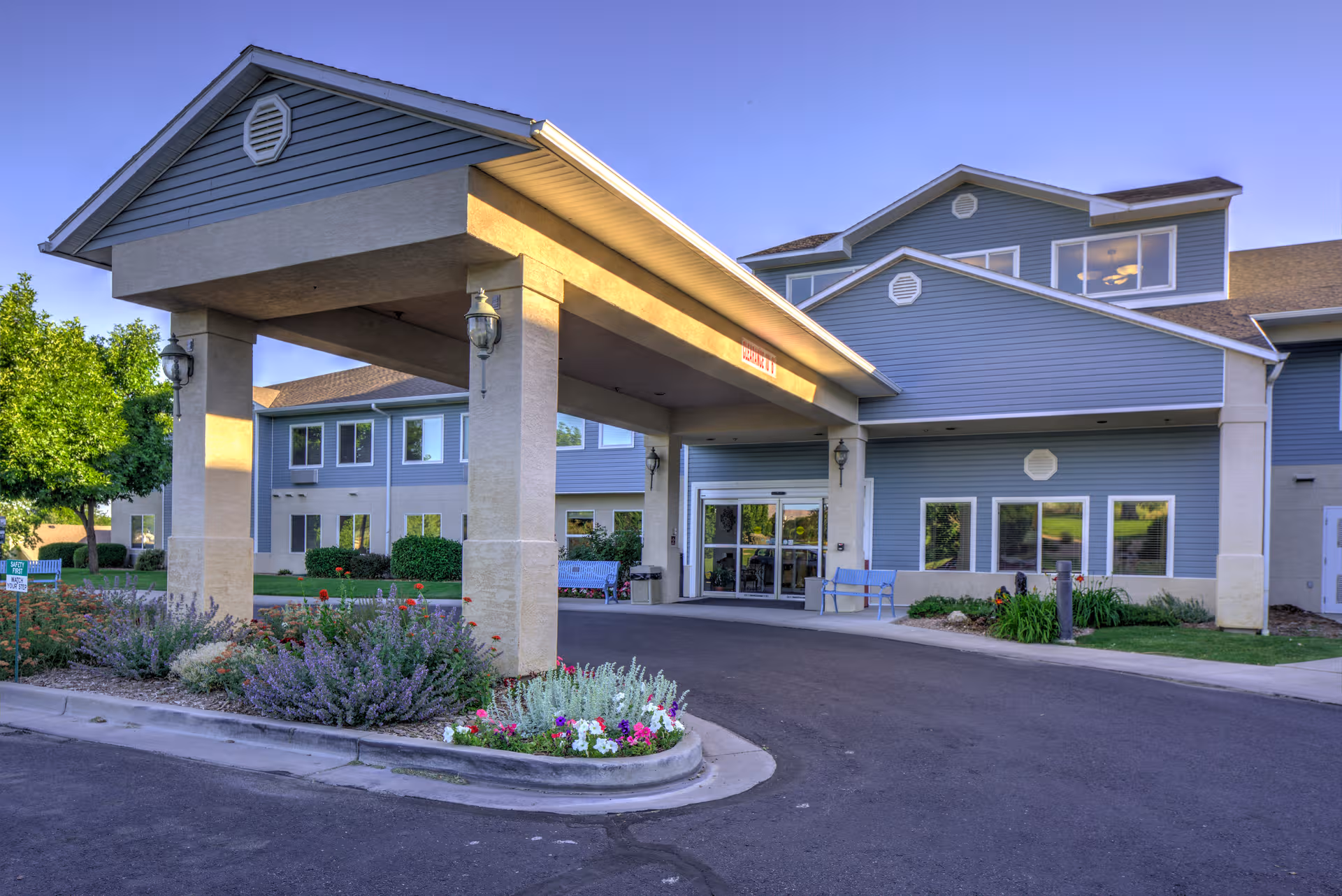 Blue, multi-story senior living facility with a wide covered entrance and manicured landscaping.