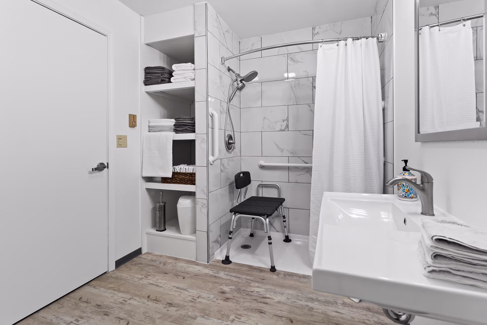 Accessible bathroom with a walk-in shower, grab bars, shelves, and sink.