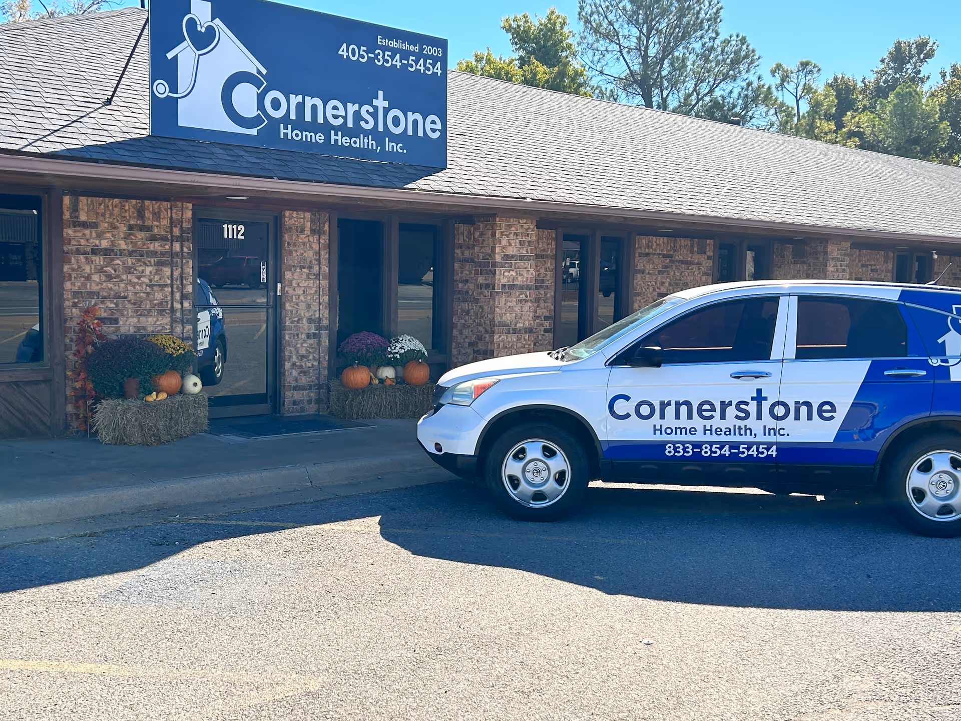 Cornerstone Home Health storefront with a branded van parked outside, pumpkins and hay bales visible.