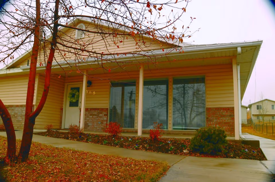 Front exterior of a single-story senior living facility with a covered entrance and large windows.