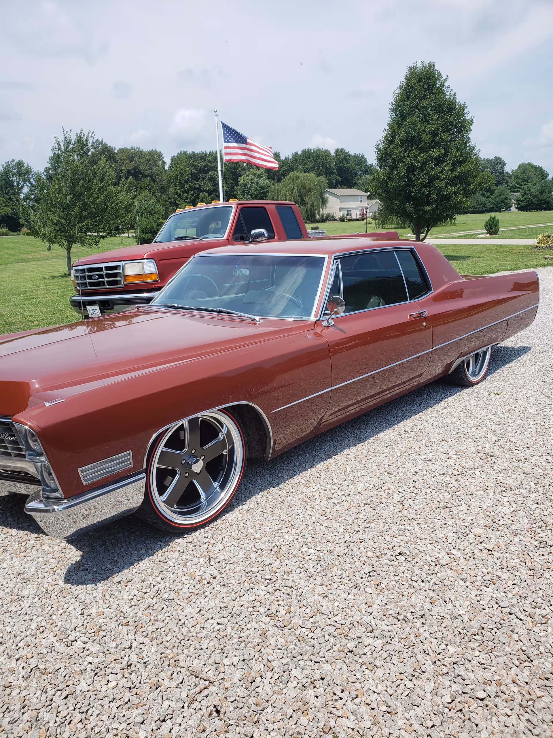 Several vintage red cars parked on a gravel lot with an American flag in the background.