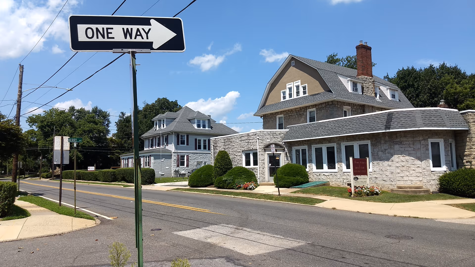 Stone-front senior living building along a quiet suburban street with a one-way sign.