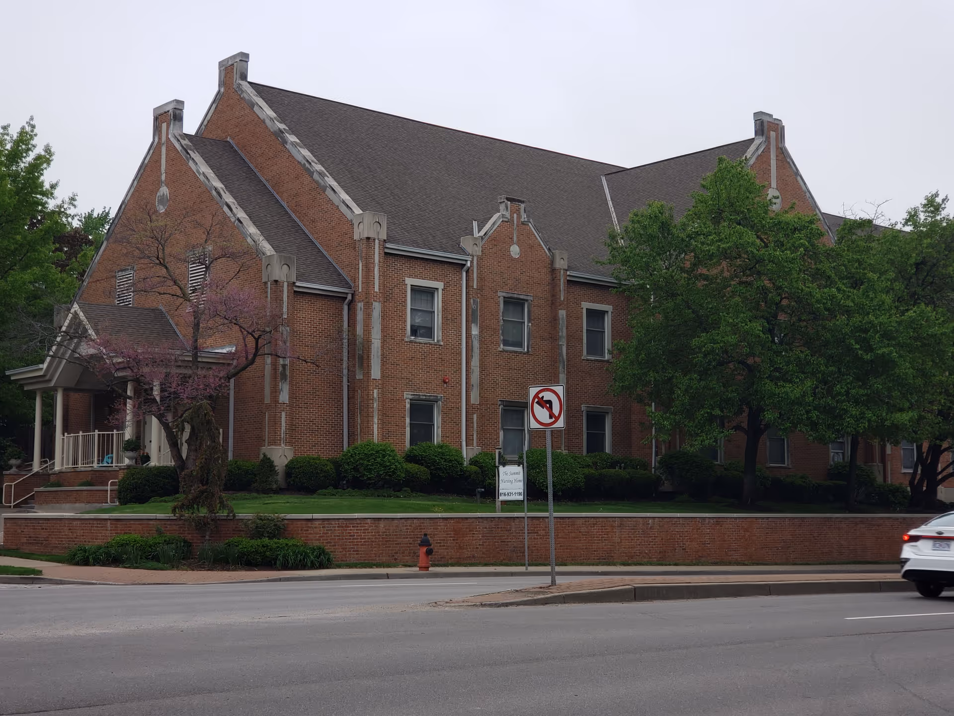 Exterior view of The Summit senior living facility, brick building with peaked roofs and trees.