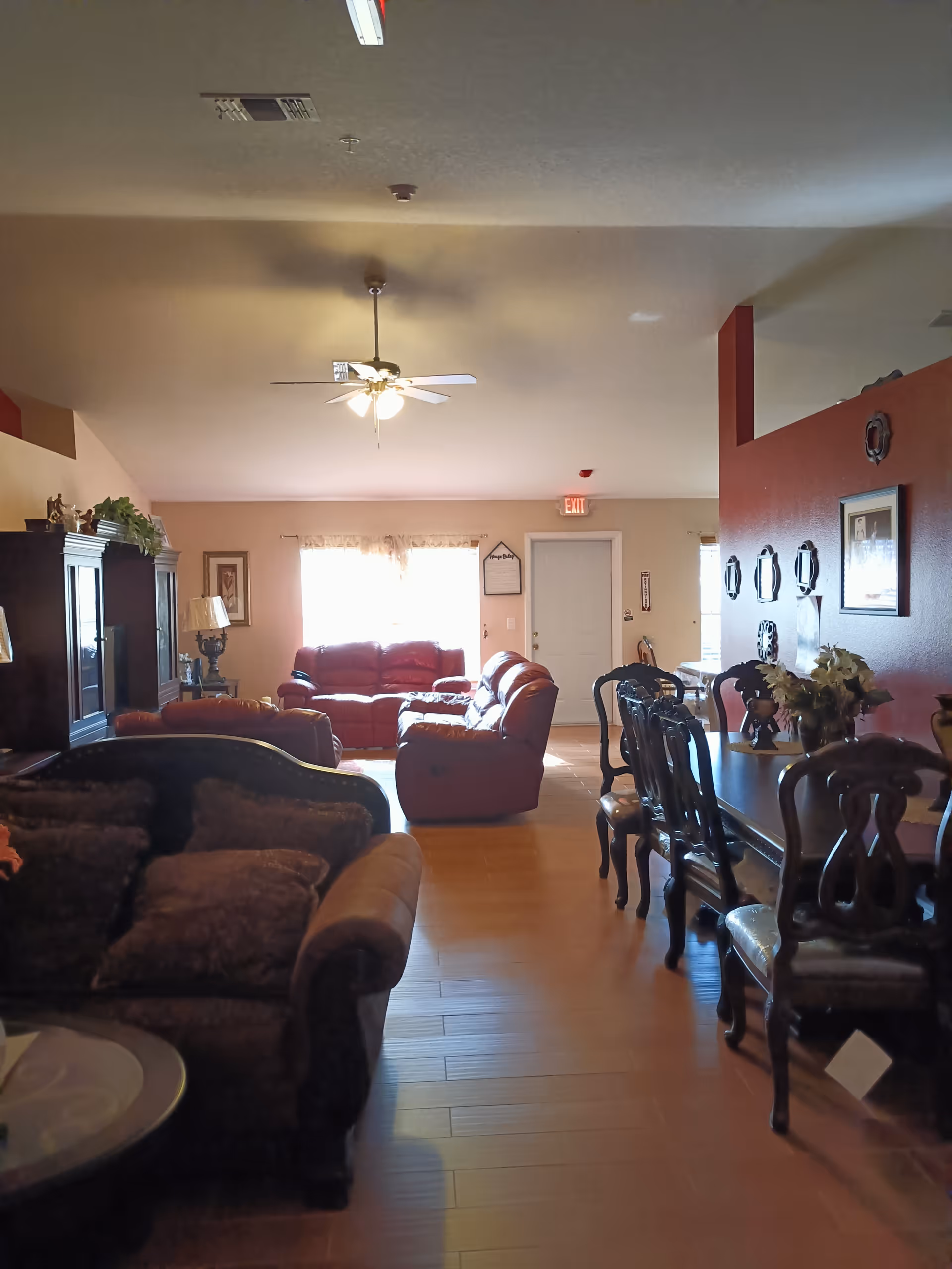 Spacious living room in a senior home with leather sofas, a dining table, and ceiling fan.