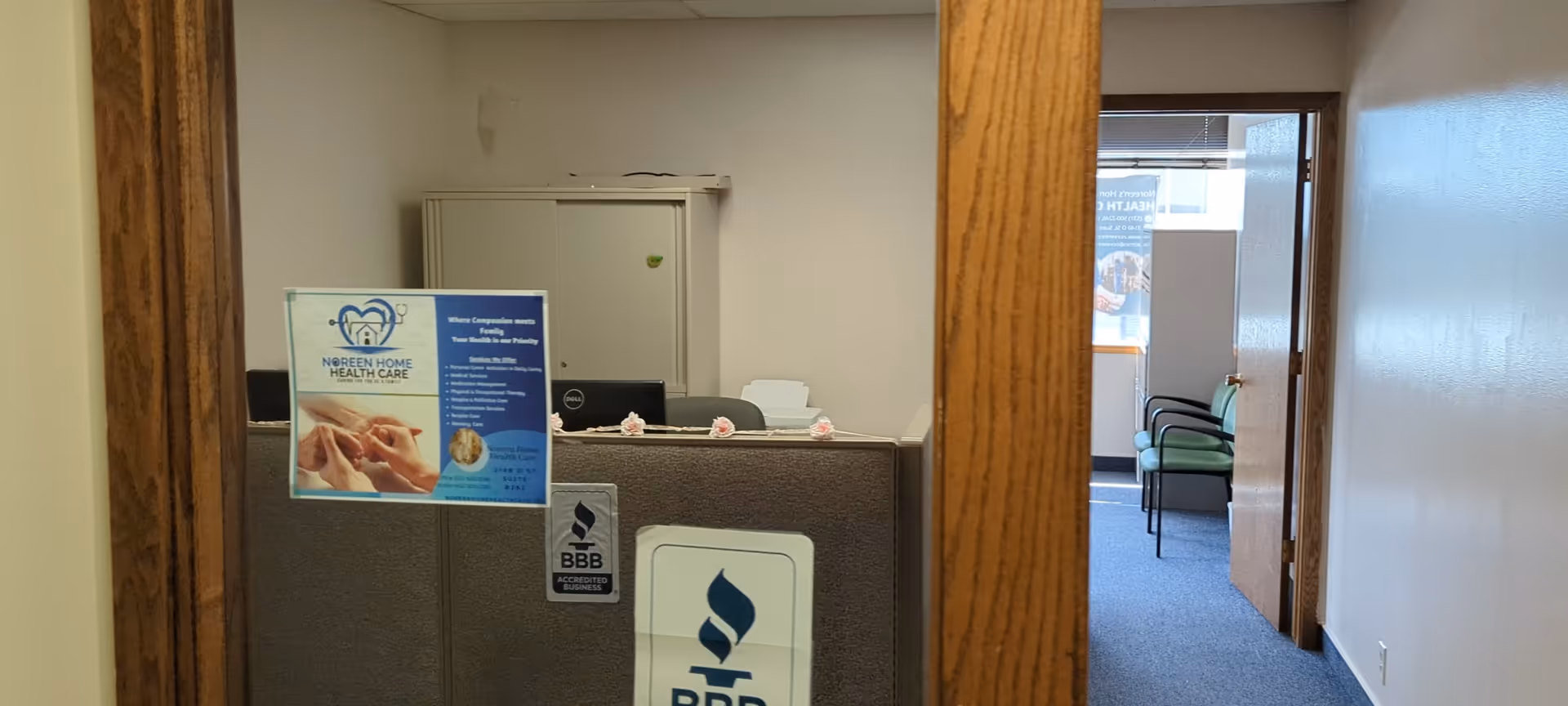 Reception desk with Noreen Home Care poster and hallway with chairs.