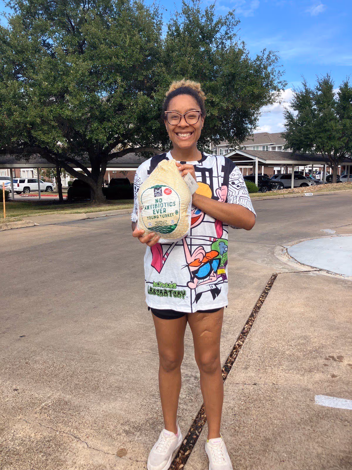 Smiling person outdoors in a parking lot holding a bag of turkey