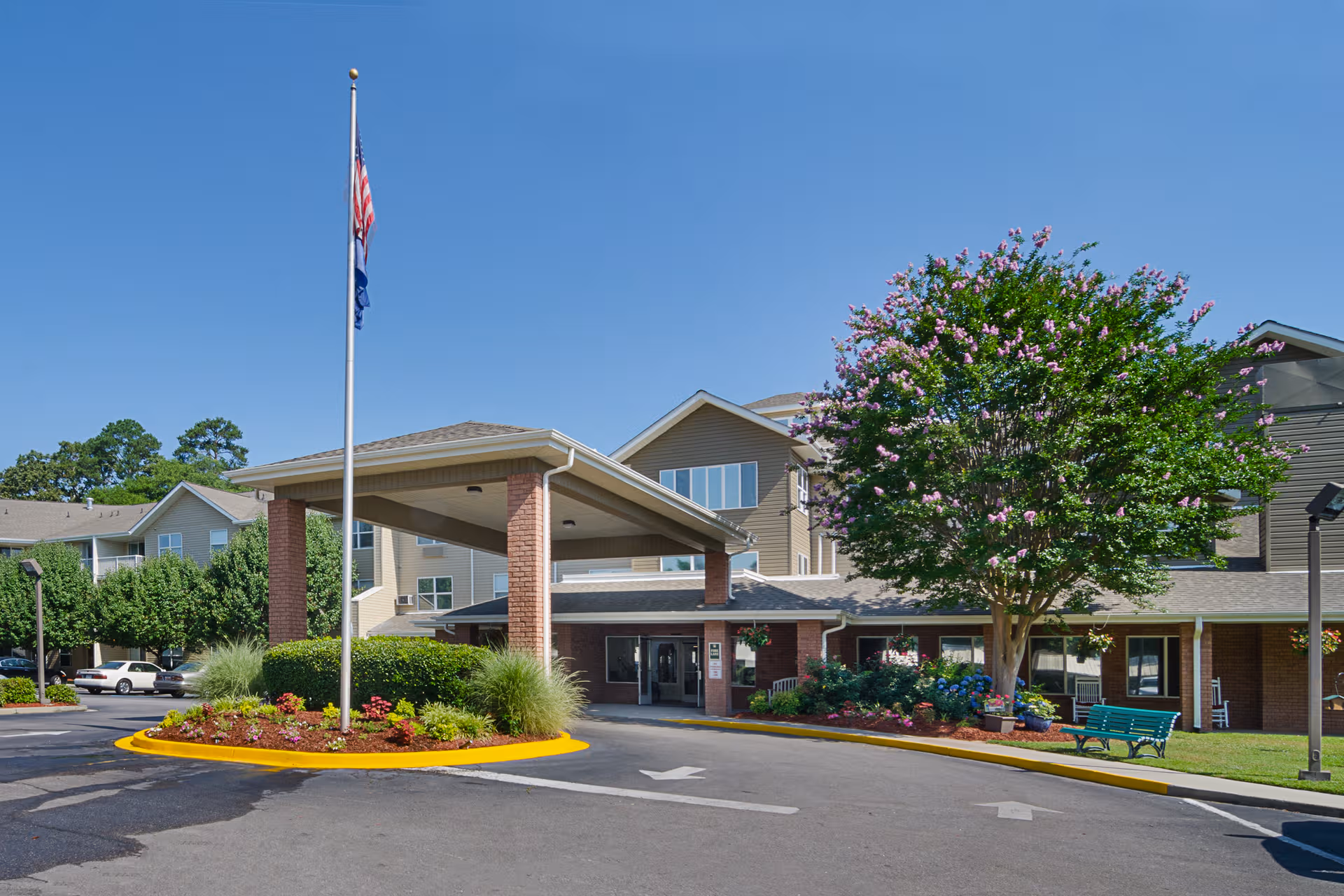 Exterior view of Holiday Columbia Pines entrance with flagpole, landscaping, and a flowering tree.
