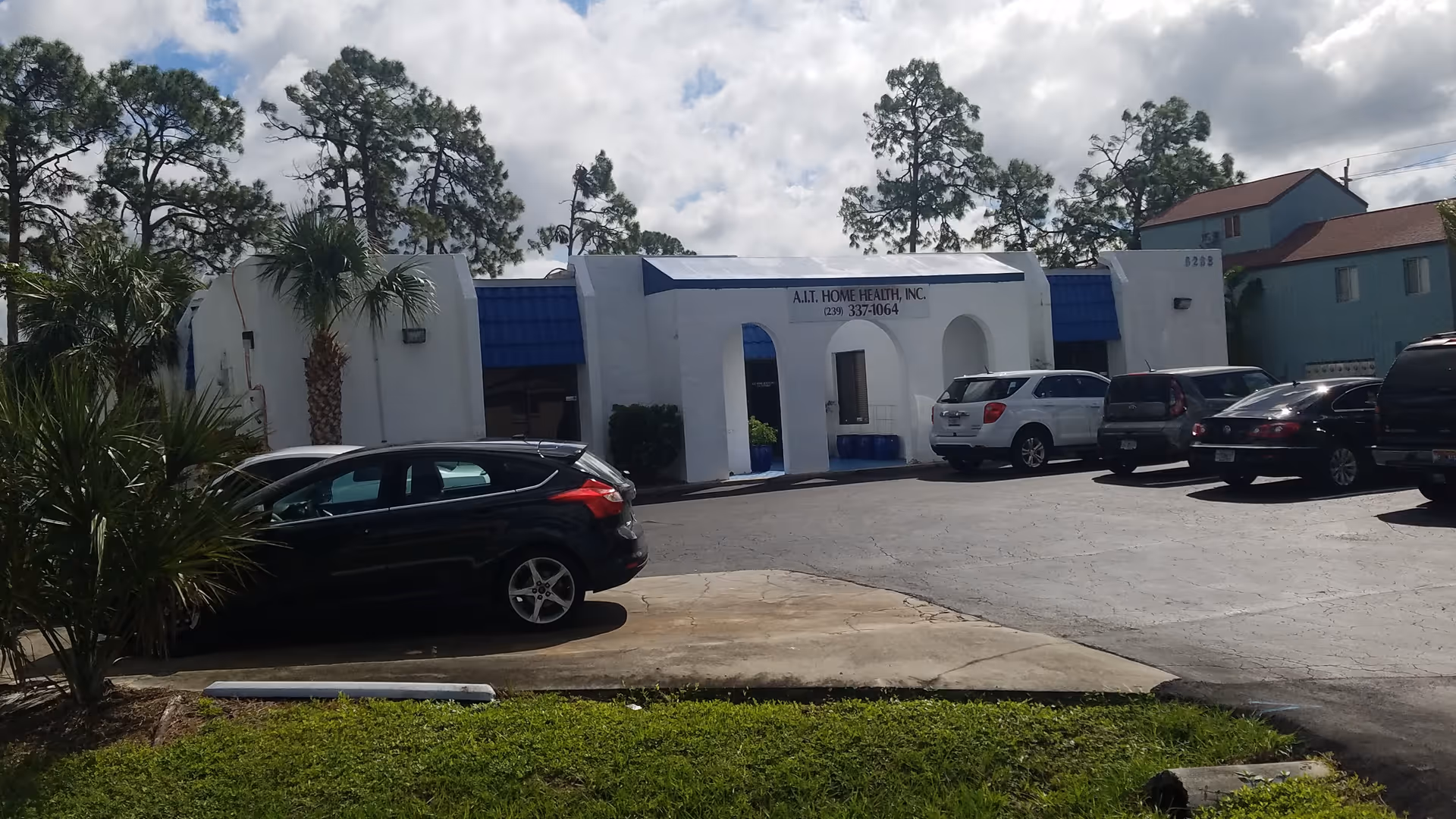 Exterior of AiT Home Health facility with blue awning and parked cars.