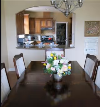 A dining room with a dark wood table, floral centerpiece, and kitchen visible through a pass-through.