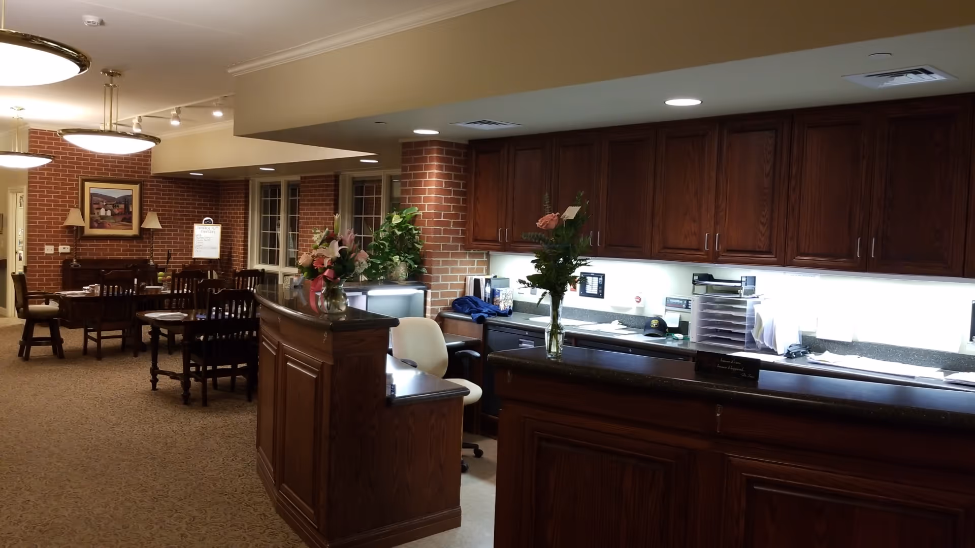 Interior common area of a senior facility with dark wood cabinetry, a counter, and dining tables.