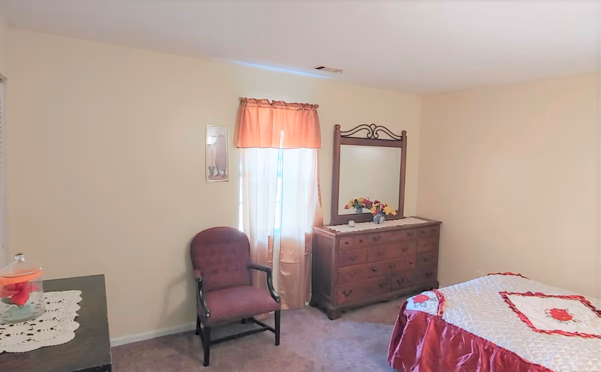 A small bedroom in a senior facility with a bed, dresser, and chair.