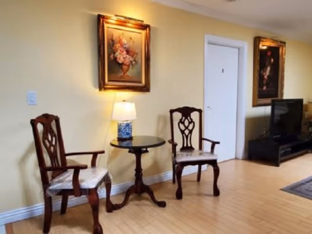 Two wooden chairs flank a round side table with a lamp in a yellow living area